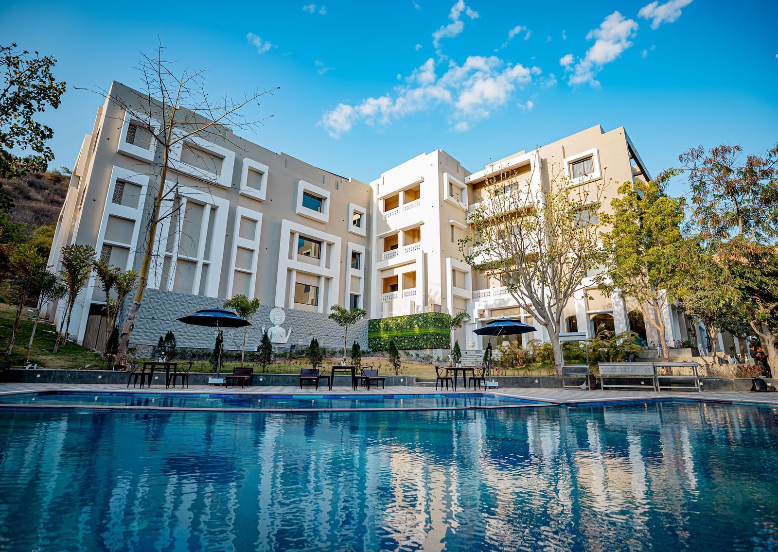 Facade view of Essentia Luxury Resort & Spa, Udaipur with a swimming pool in the foreground.