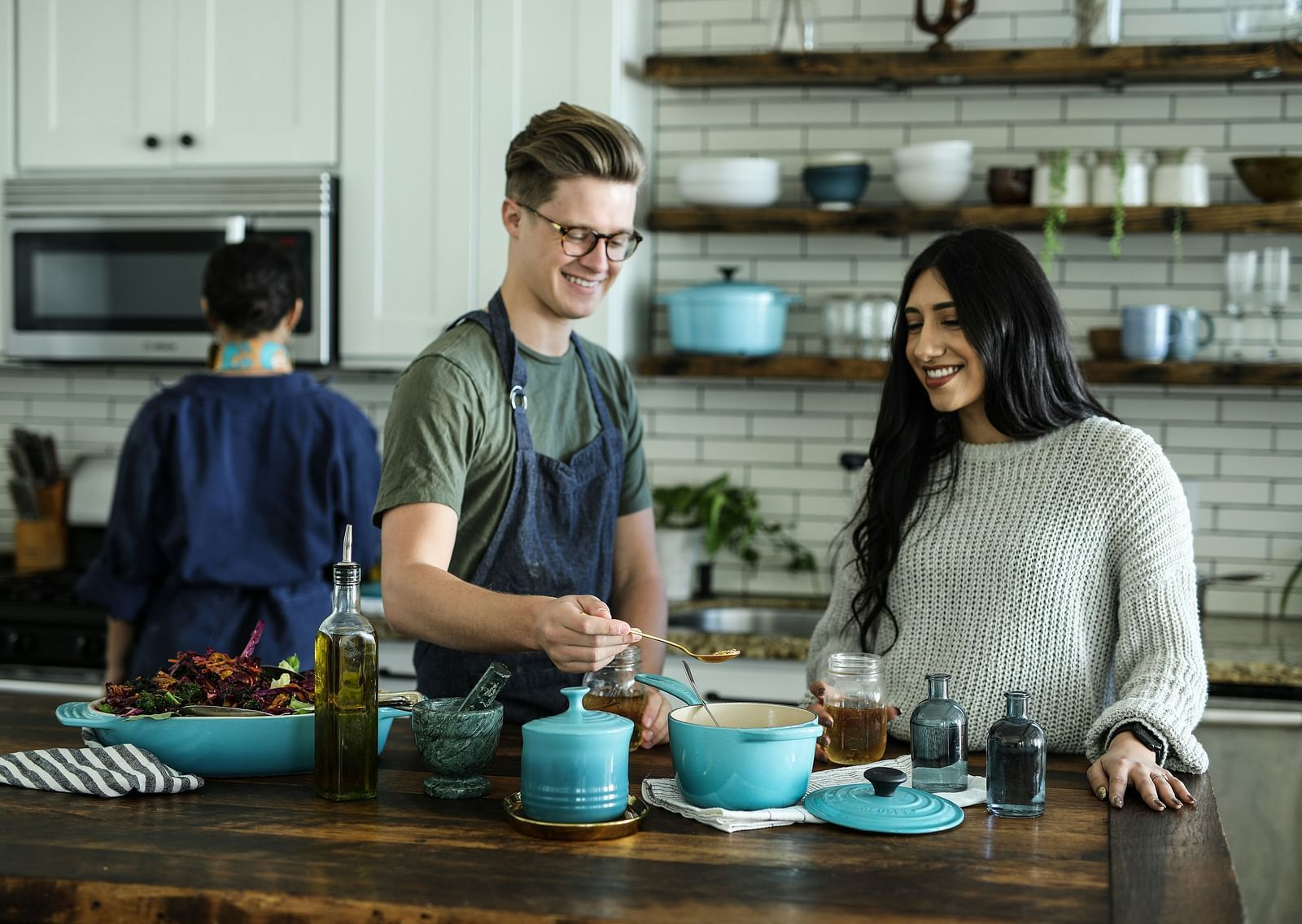 An overview of a cooking class with a man wearing an apron standing next to a woman in the kitchen.
