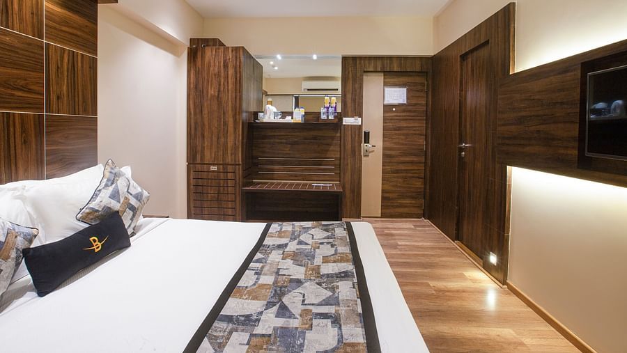 A side angle view of the Deluxe Hotel Bawa Regency, Dadar focusing on the comfy bed, wardrobe, and kettle with sugar and other amenities.