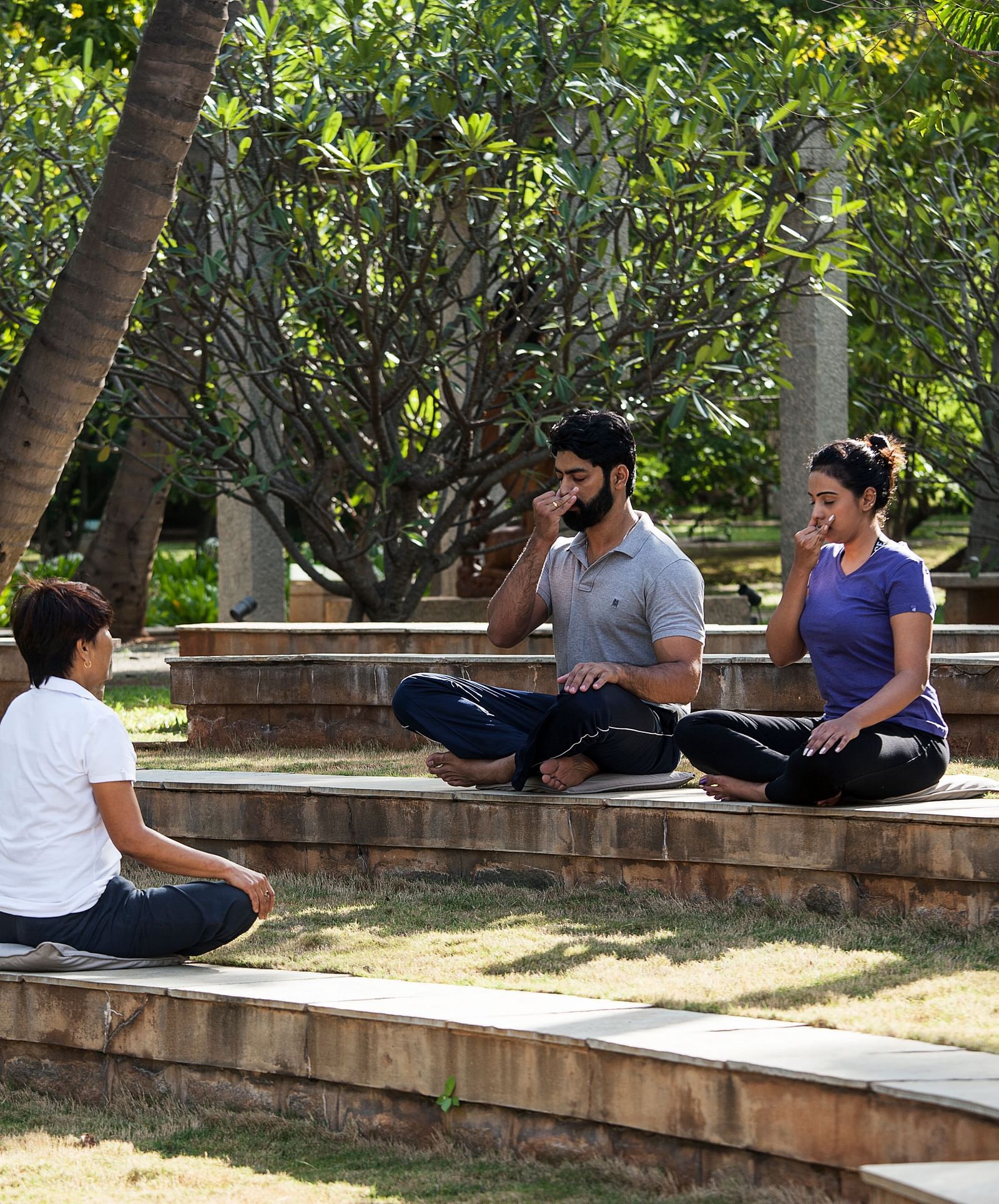 People sitting on steps outdoors, trees, performing yoga - Shreyas Retreat