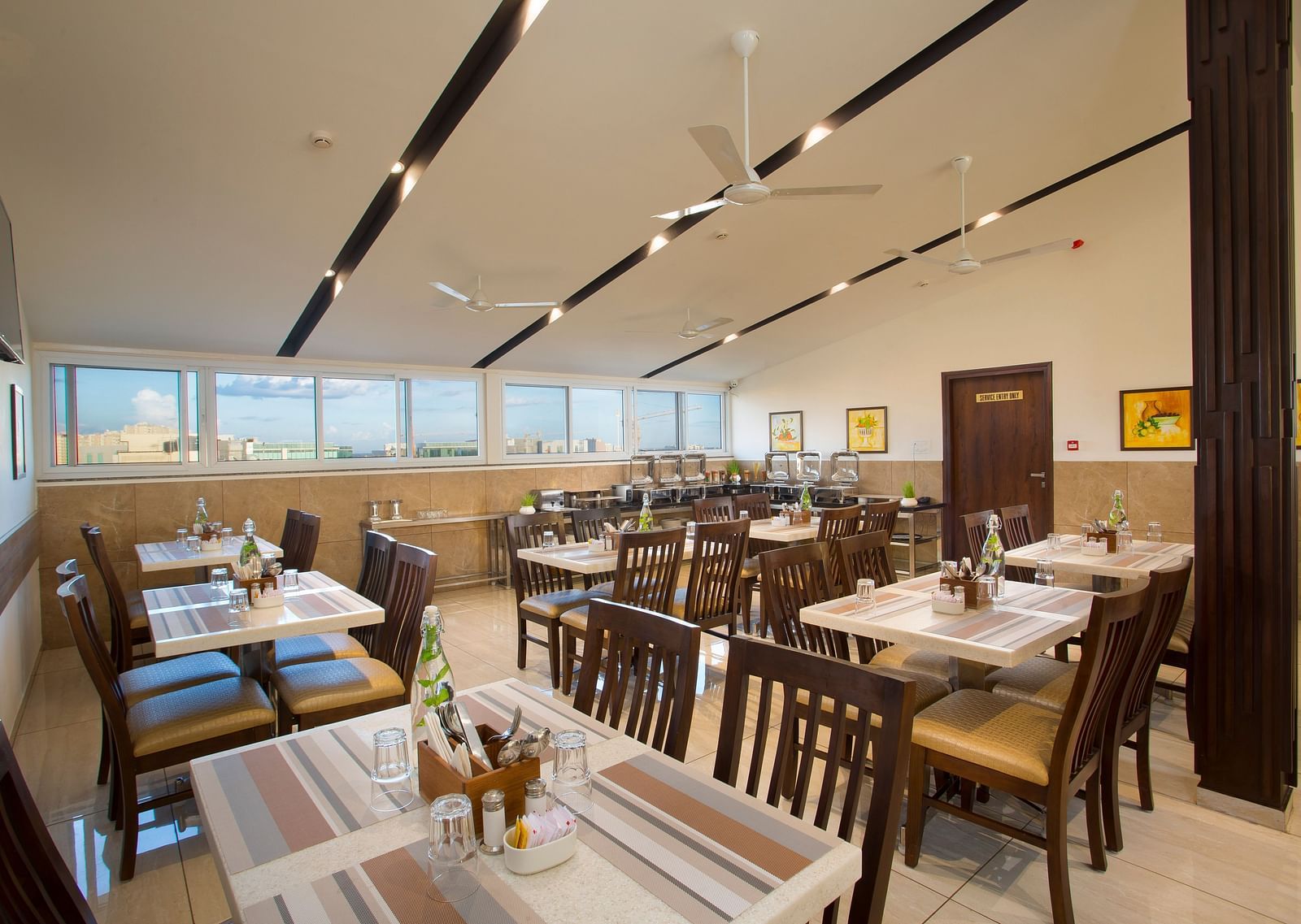 A hotel restaurant with wooden tables and chairs, large windows and ceiling fans - De Venetian by TGI, Brookefield