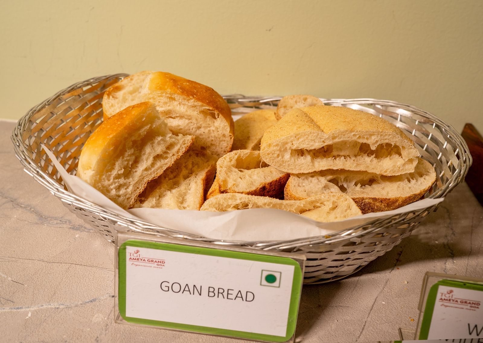 A basket of sliced Goan bread on a buffet table with a label in front - TGI Ameya Grand, Goa