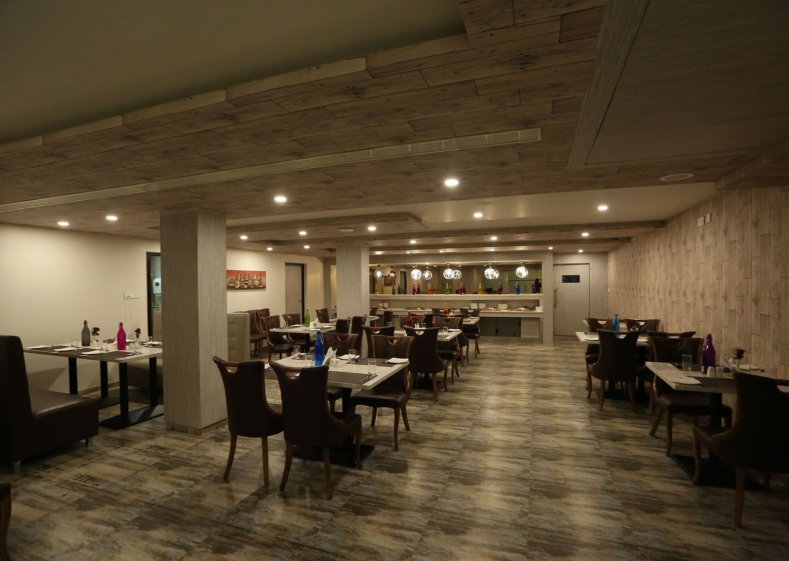 A long, spacious restaurant with tables and chairs, illuminated by ceiling lights - TGI SPS Grand, Coimbatore