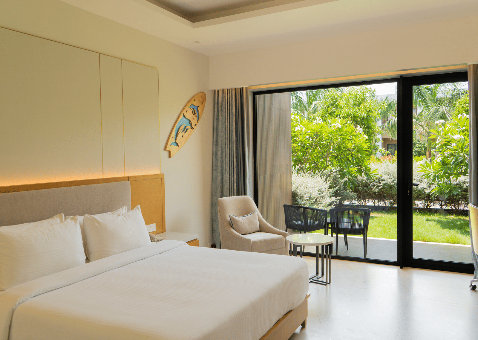 Garden Courtyard room at The Shore Trishvam, Pondicherry, with floor-to-ceiling glass doors opening to a lush tropical garden and outdoor seating.