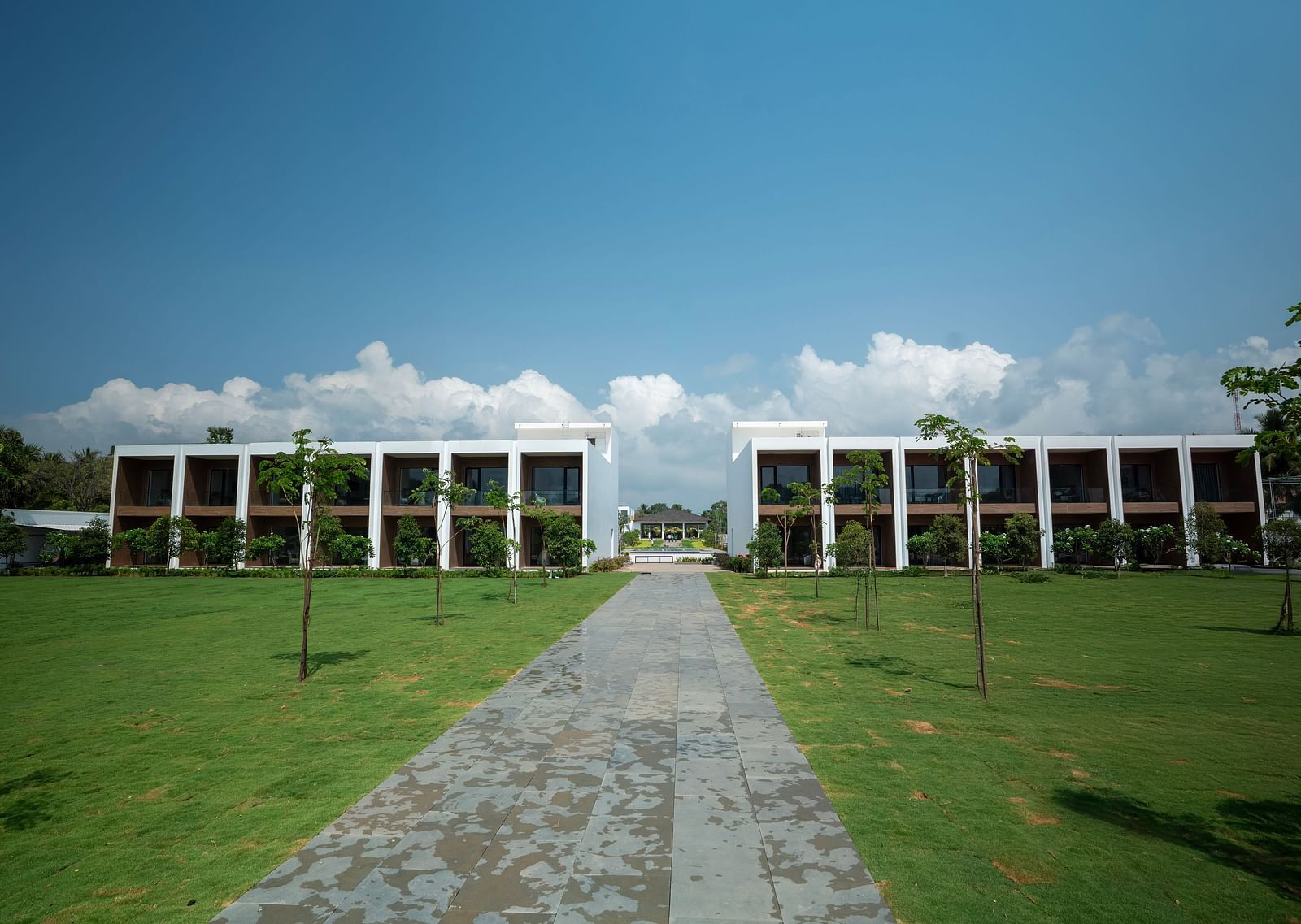  A lush green lawn at The Shore Trishvam, Pondicherry divided by a pathway in the middle with a clear blue sky in the background.