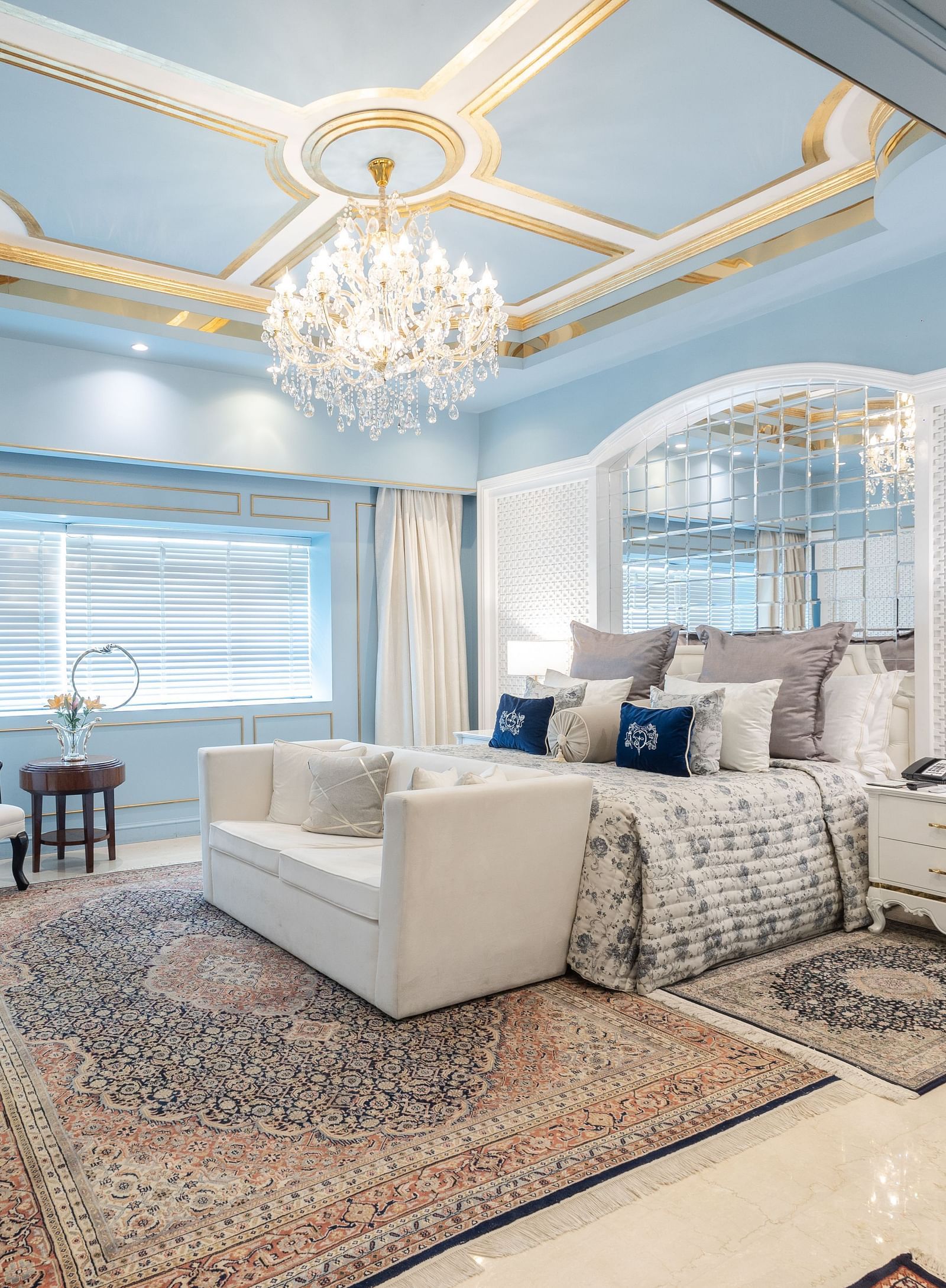An image of a suite with a large bed and a sofa placed in front of a television and a chandelier hanging from the ceiling