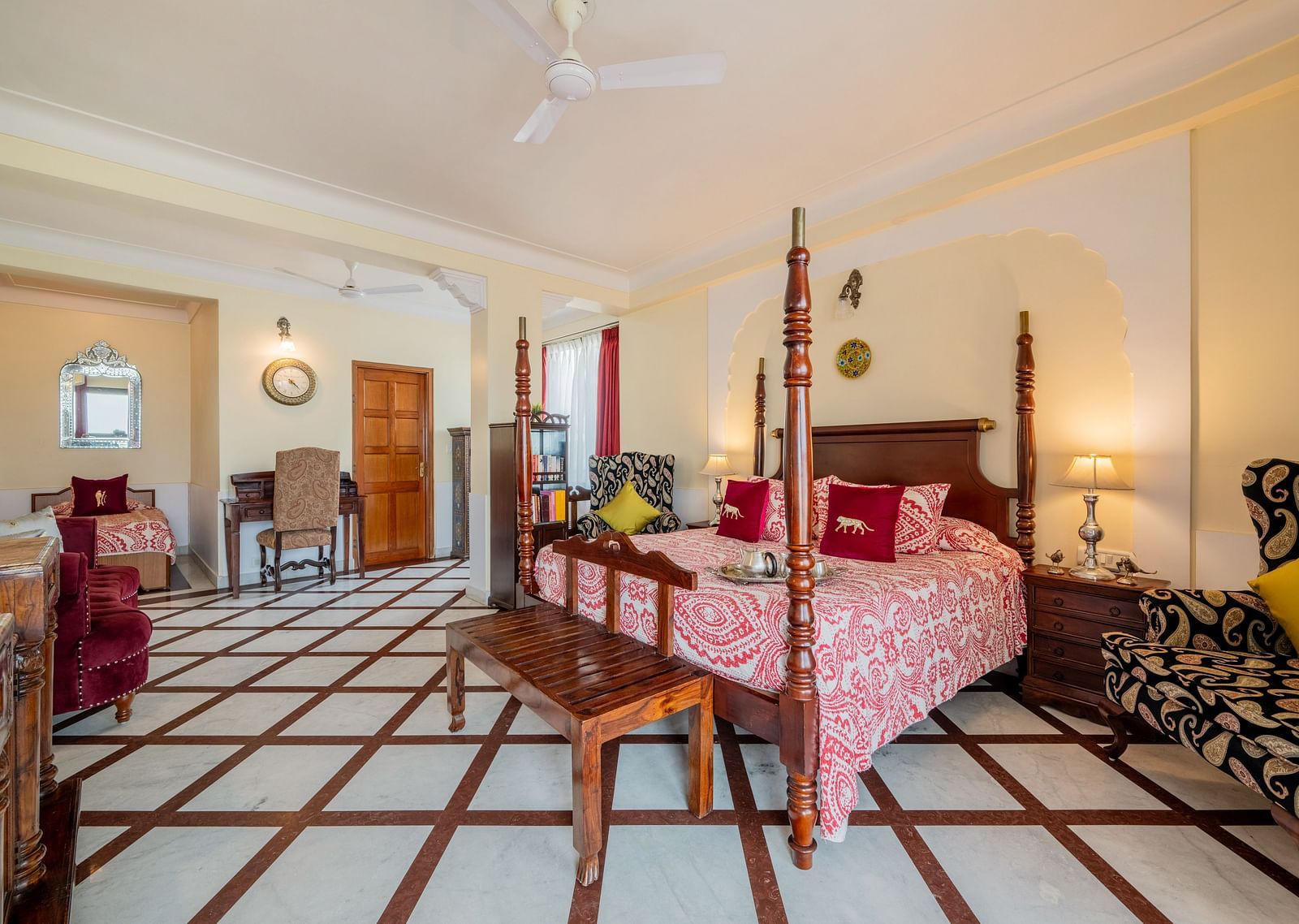 A spacious suite at Dera Rawatsar, Jaipur, includes a four-poster bed, a seating area with a sofa, a dining table, and unique tiled flooring.