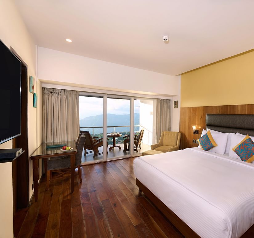 A room featuring a bed, a side drawer, a TV and a balcony with seating arrangements - Renest Dunsvirk Court Mussoorie
