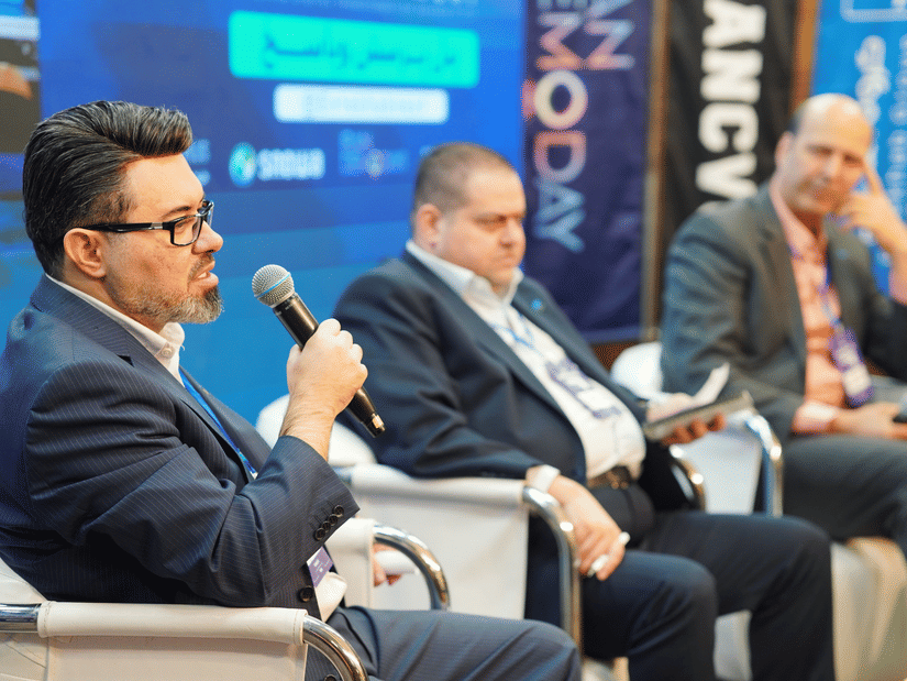 Side-angle view of 3 panellists dressed in business formals sitting on chairs addressing an audience.