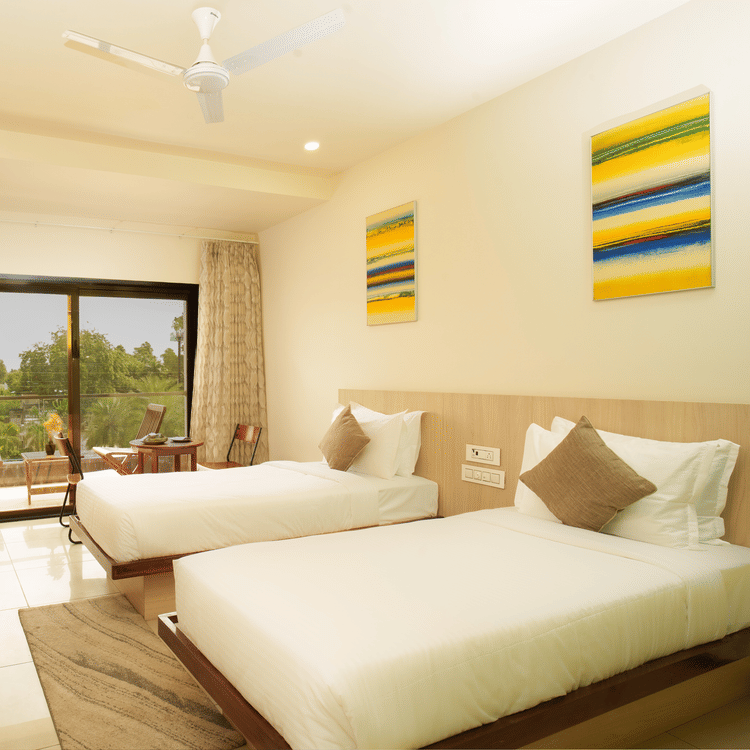 Hotel room with three beds, a television, and brightly coloured artwork at Arawali Ananta Elite, Jaipur.