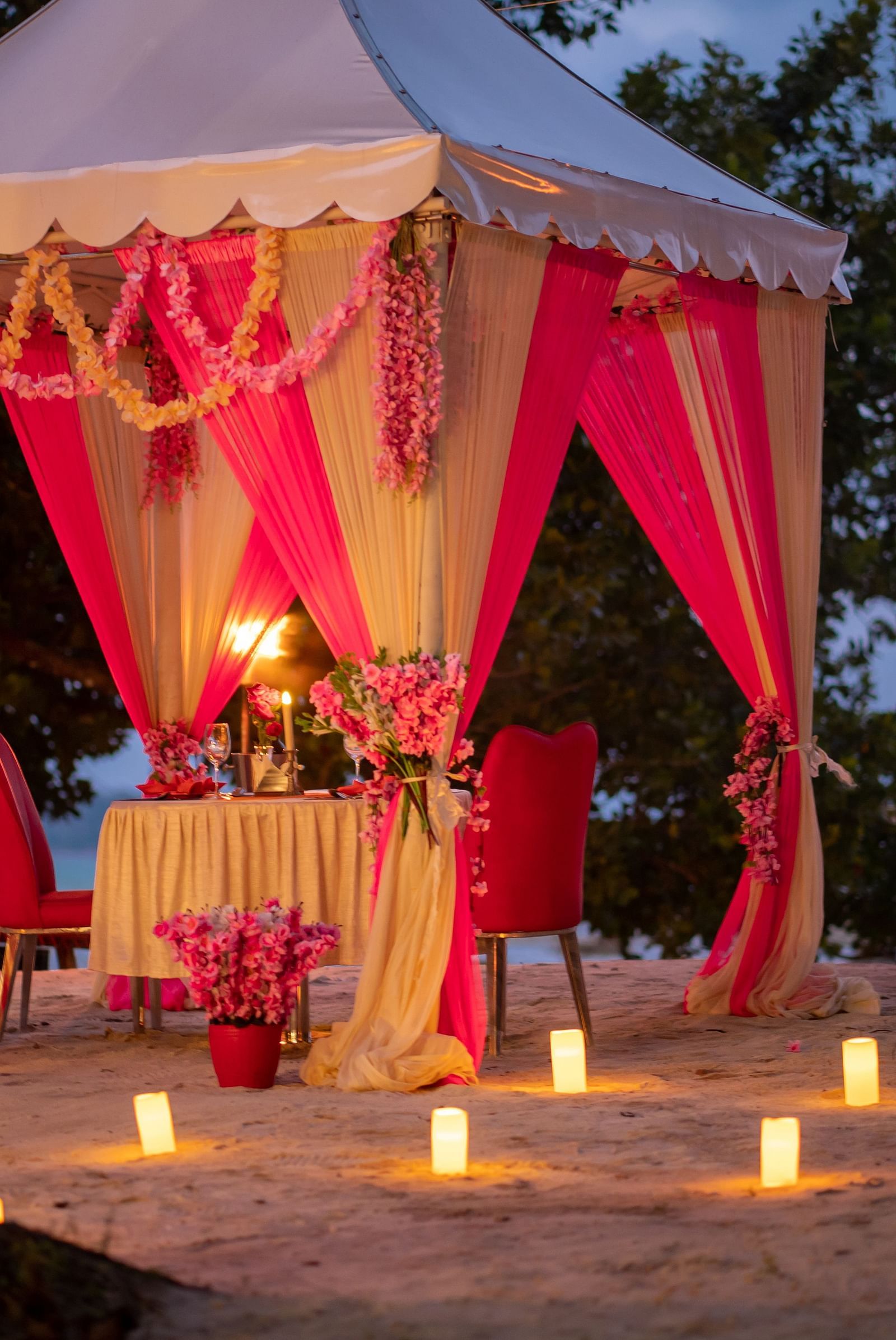 Intimate dining setting on a beach with a candle-lit table and a festively decorated tent - Coral Reef Resort & Spa, Havelock