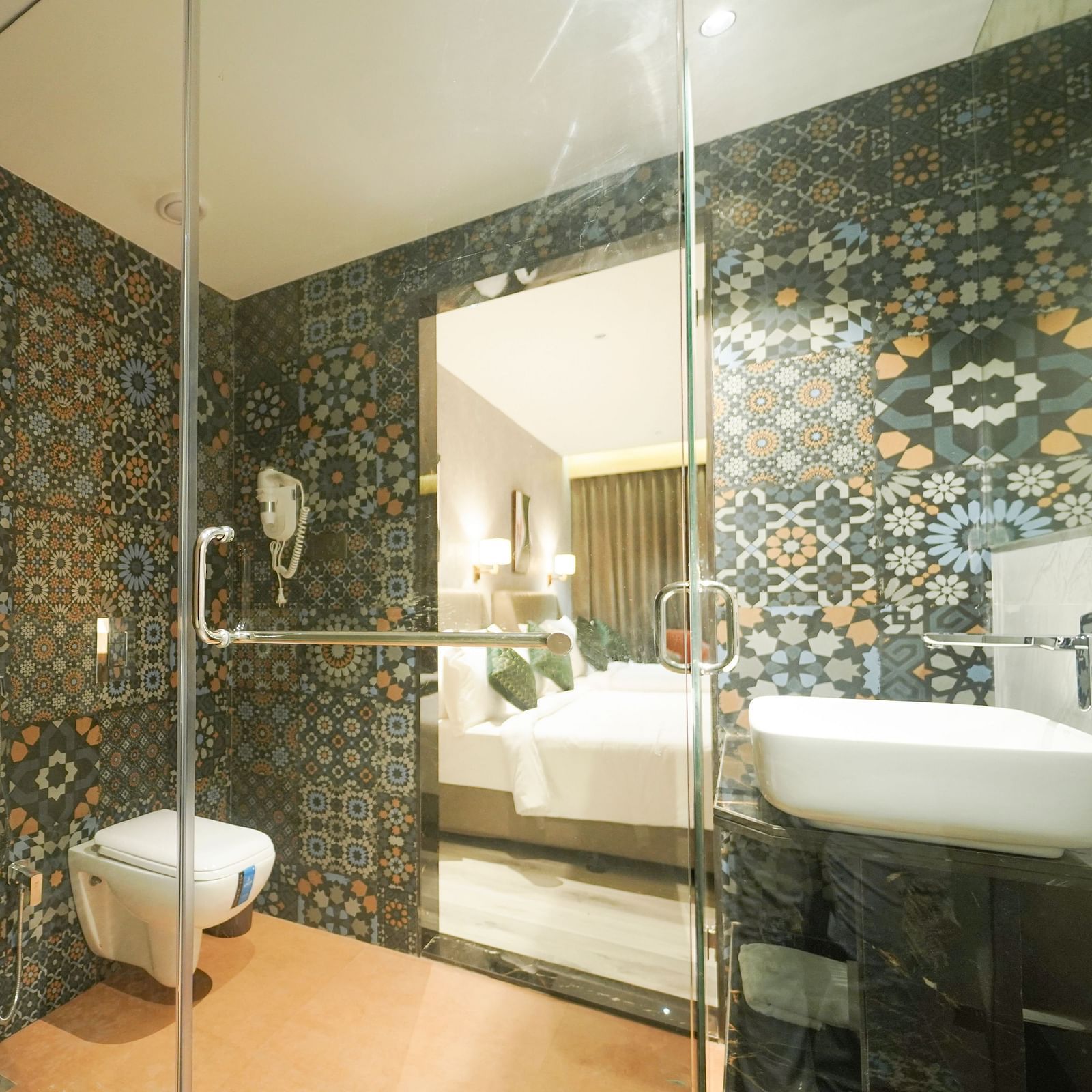 A bathroom with patterned tiles features a shower area with a glass door, a toilet, and a sink with a mirror - Hotel Park Inn, Nellore.