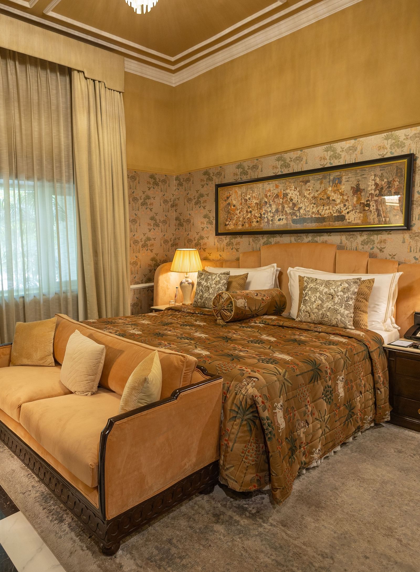 Executive Suite at The Claridges New Delhi, featuring a cosy king sized bed, a sofa placed in front, and a bedside lamp