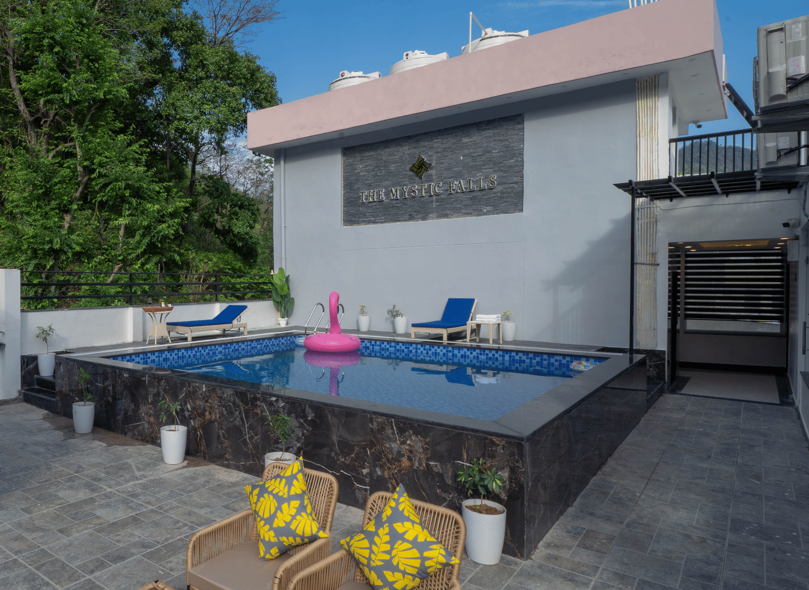 A terrace with a swimming pool, a railing, wicker furniture, and a building exterior visible in Perfectstayz Premium Mystic Falls, Rishikesh.