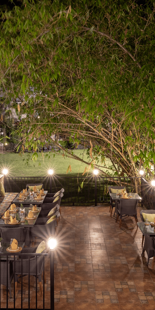 A dimly lit outdoor dining setting at night, with multiple tables illuminated by warm lights at The Golden Tusk, Jim Corbett