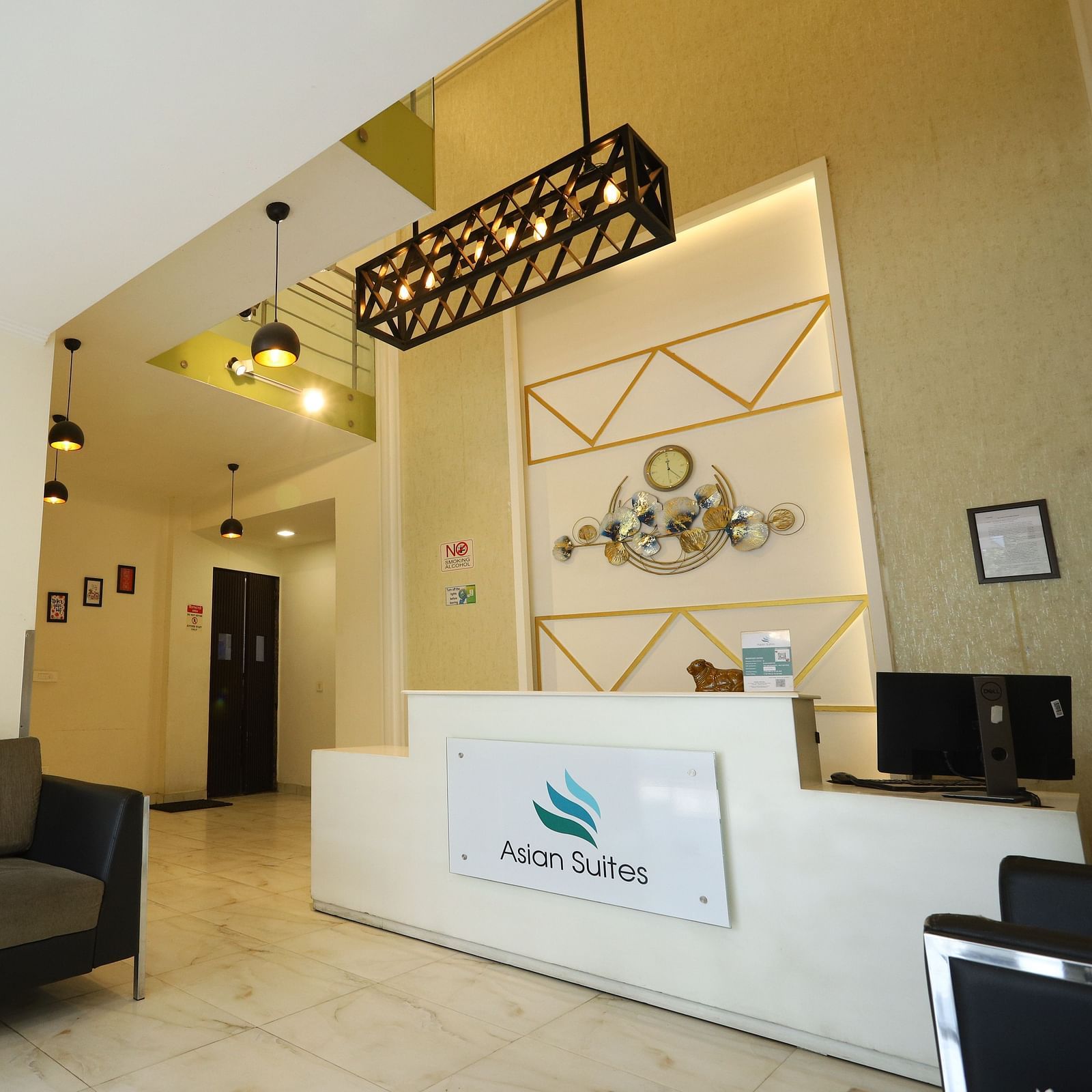 A reception area with a dark sofa and a white counter featuring a logo, illuminated by modern lighting fixtures - Asian Suites Cyber Park, Gurgaon