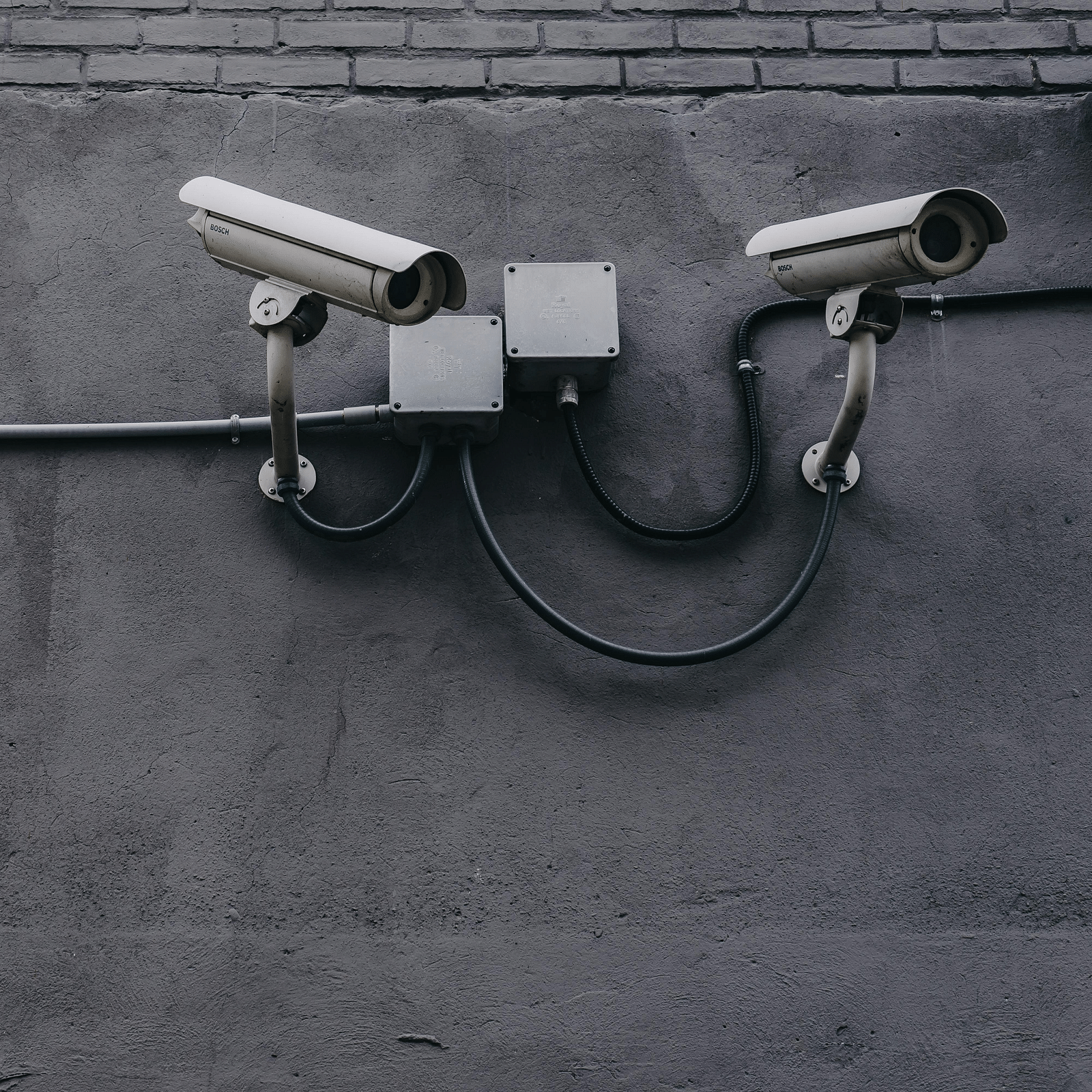 Two gray bullet security cameras hung on a cement wall.