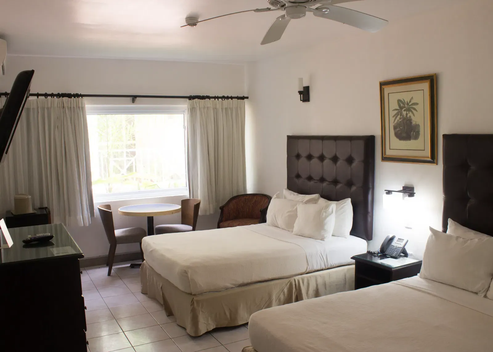 A spacious hotel room features two large beds, a sitting area with a table and chairs, and a window with curtains | Executive Double Room| Altamont Court, Jamaica