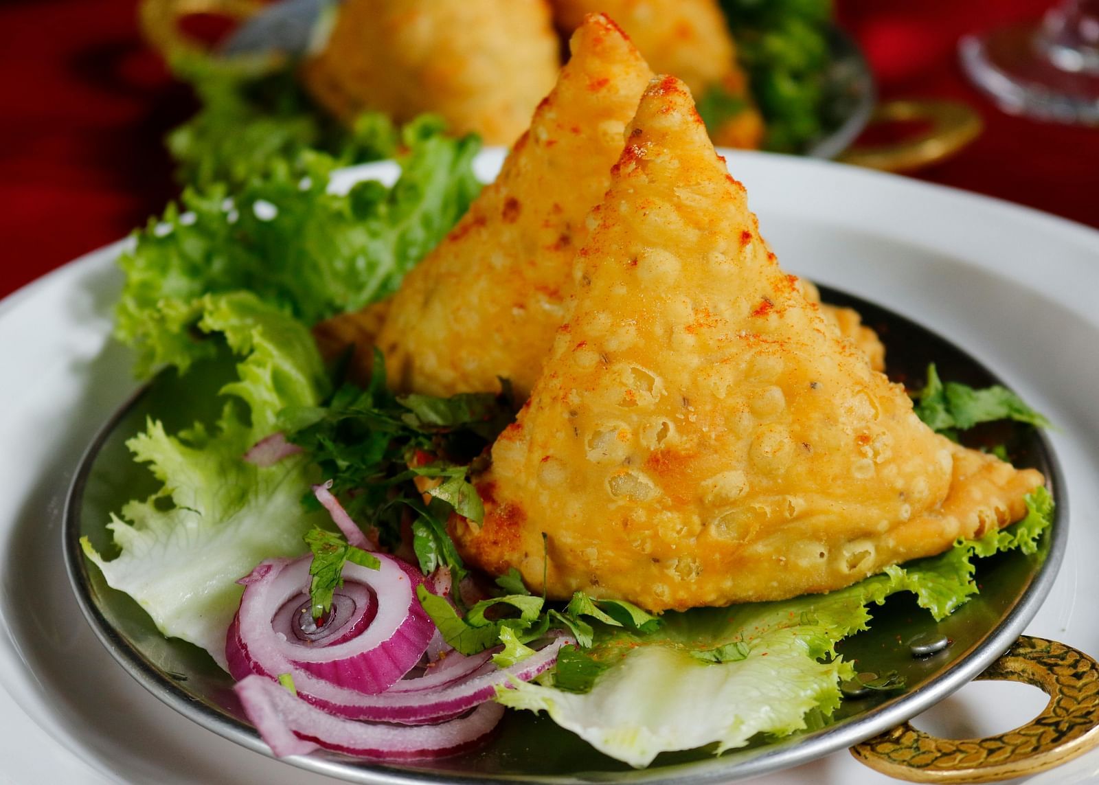 Two samosa's served on a platter with onion and lettuce on the side.