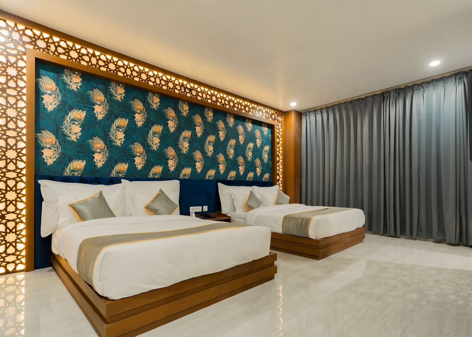 A bedroom at the Bamboo Saa Mulberry Resort featuring two twin beds with white linens and gray throws. A decorative wall panel with a blue and gold pattern is above the beds.
