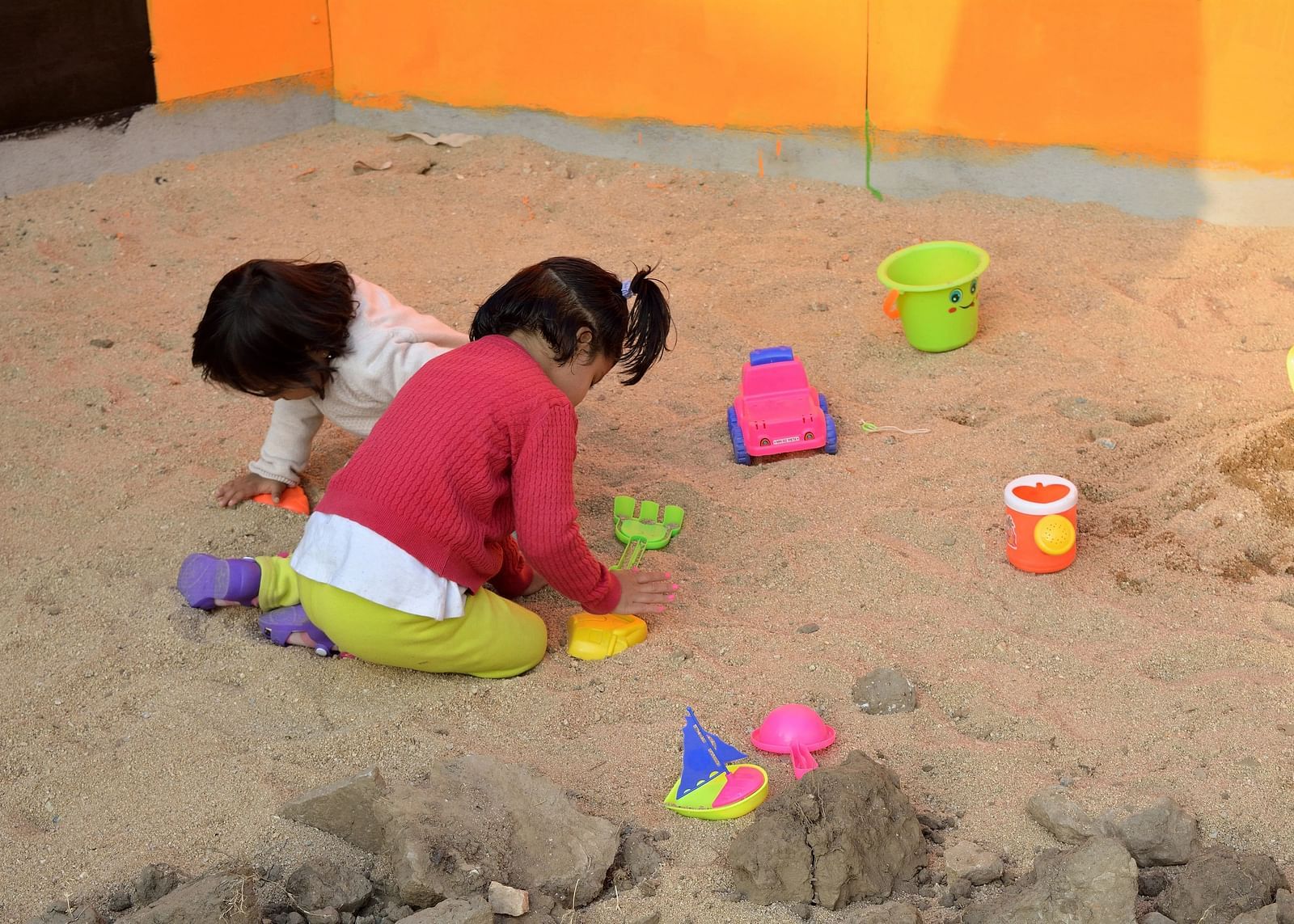 Two kids playing with toys in a sandbox.