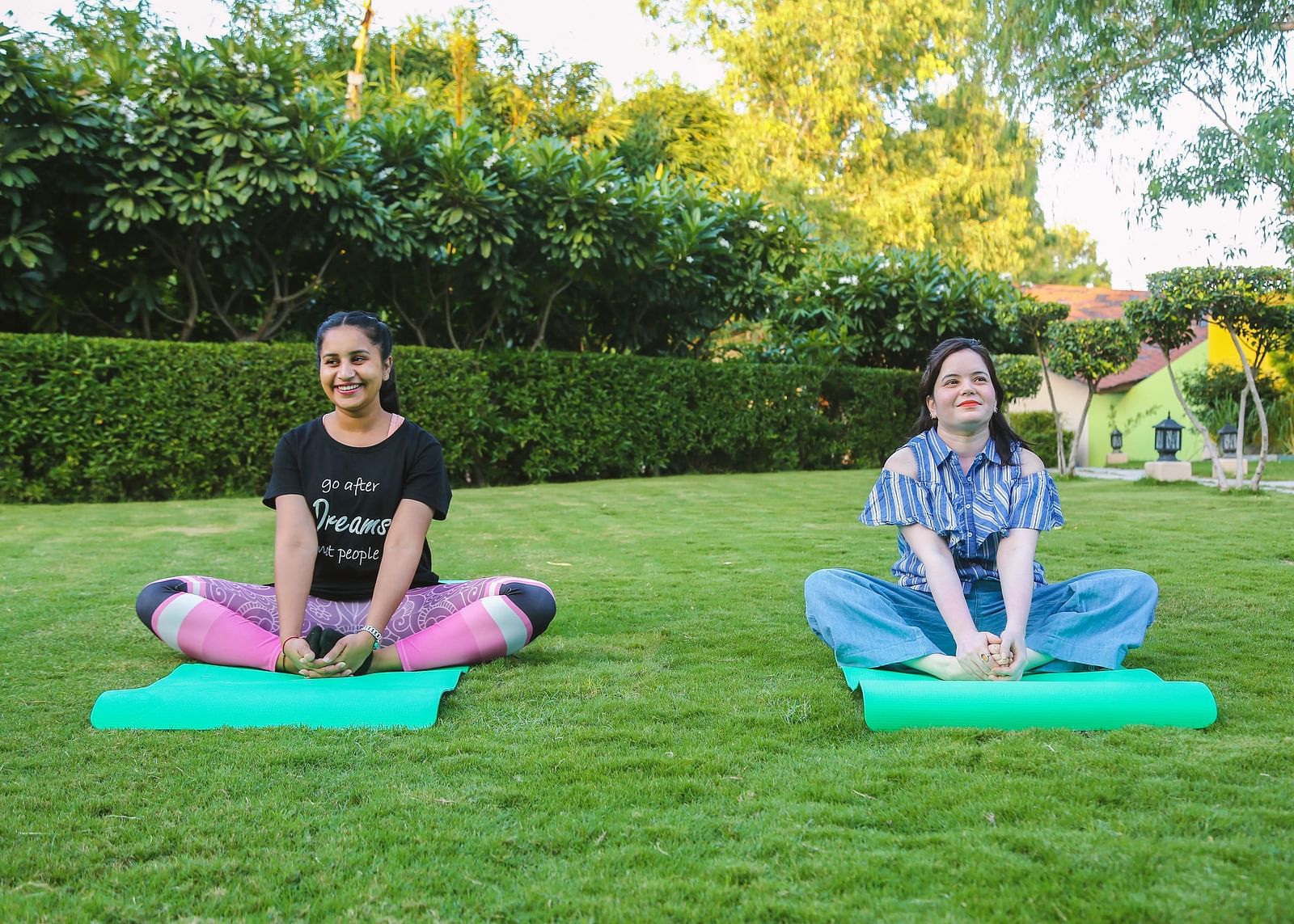 Two women meditating on yoga mats in a green garden.