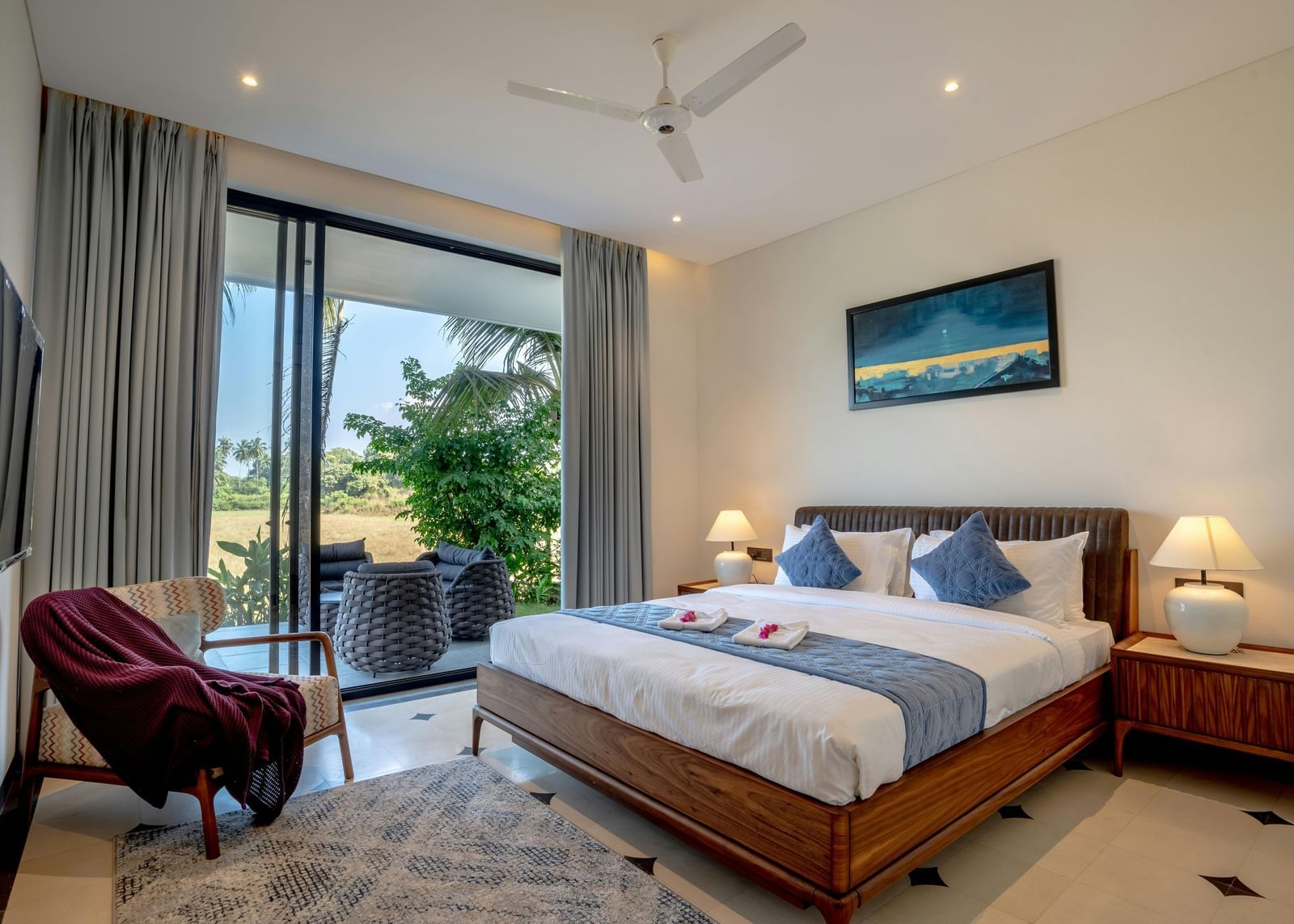 A room with balcony at Bamboo Saa Sunrrise Wedding and Wellness Resort, Jaipur, featuring a spacious bed with bedside tables and lamps, artwork above the headboard, and outdoor view through glass doors.