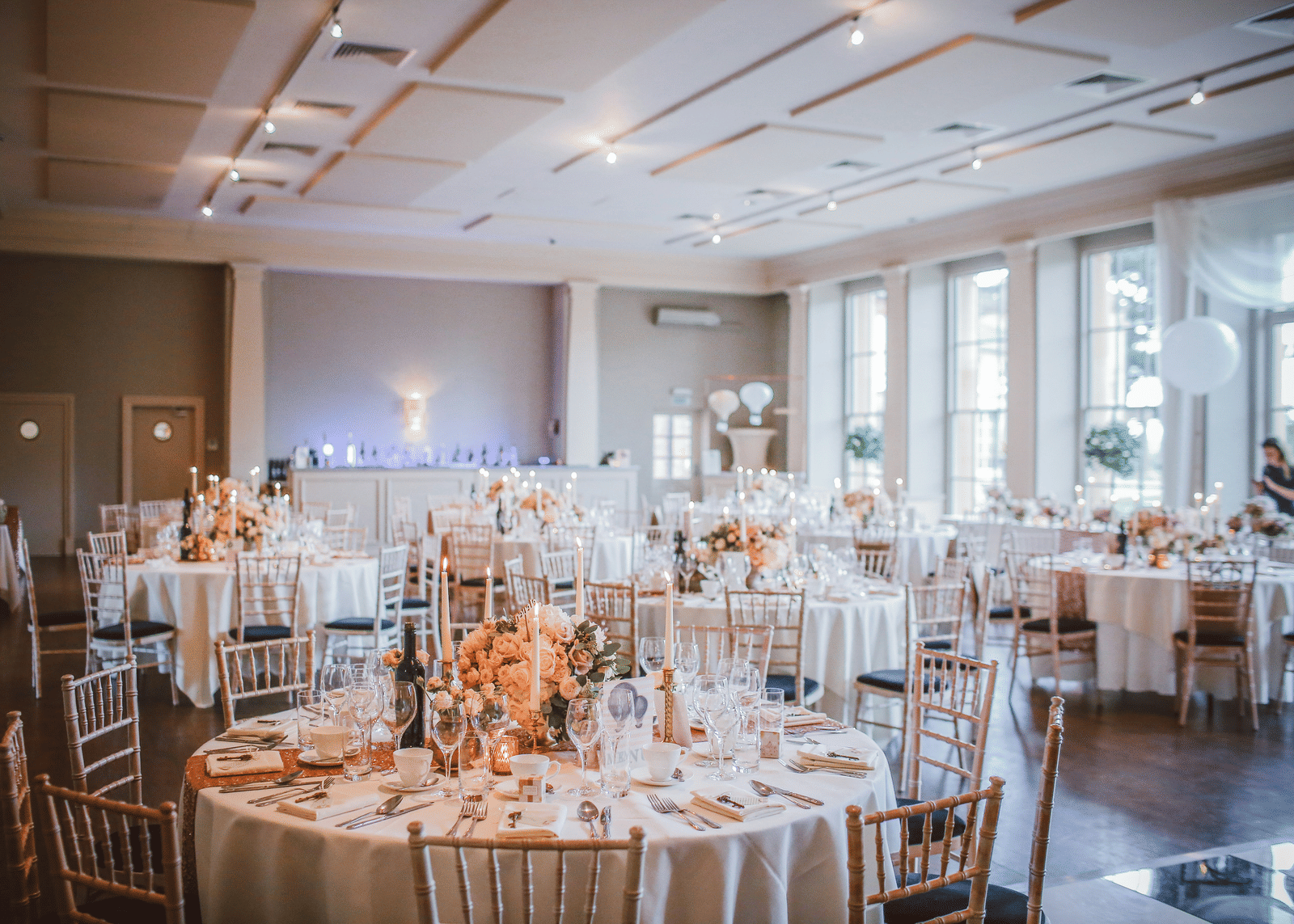 A spacious event hall with natural light, floral centre pieces, and stylish seating for formal gatherings.