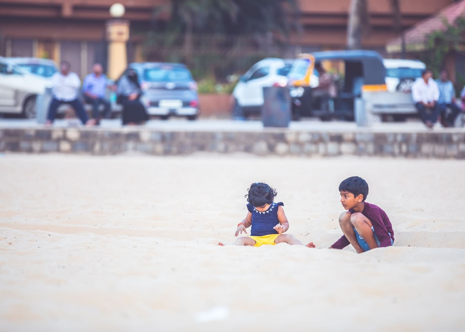 Children playing in the sand on the beach with cars parked in the backdrop