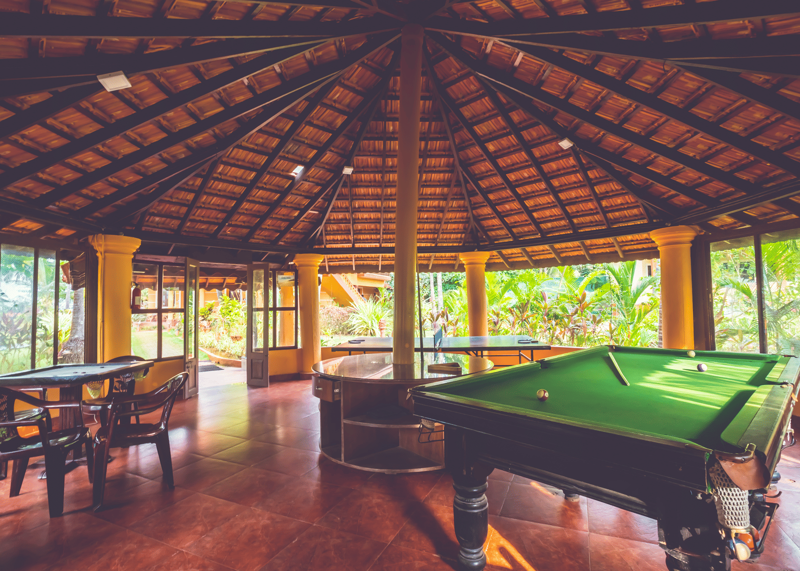 Open-sided hut with a tiled roof, containing a green snooker table and wooden seating at Paradise Lagoon Resort, Udupi.