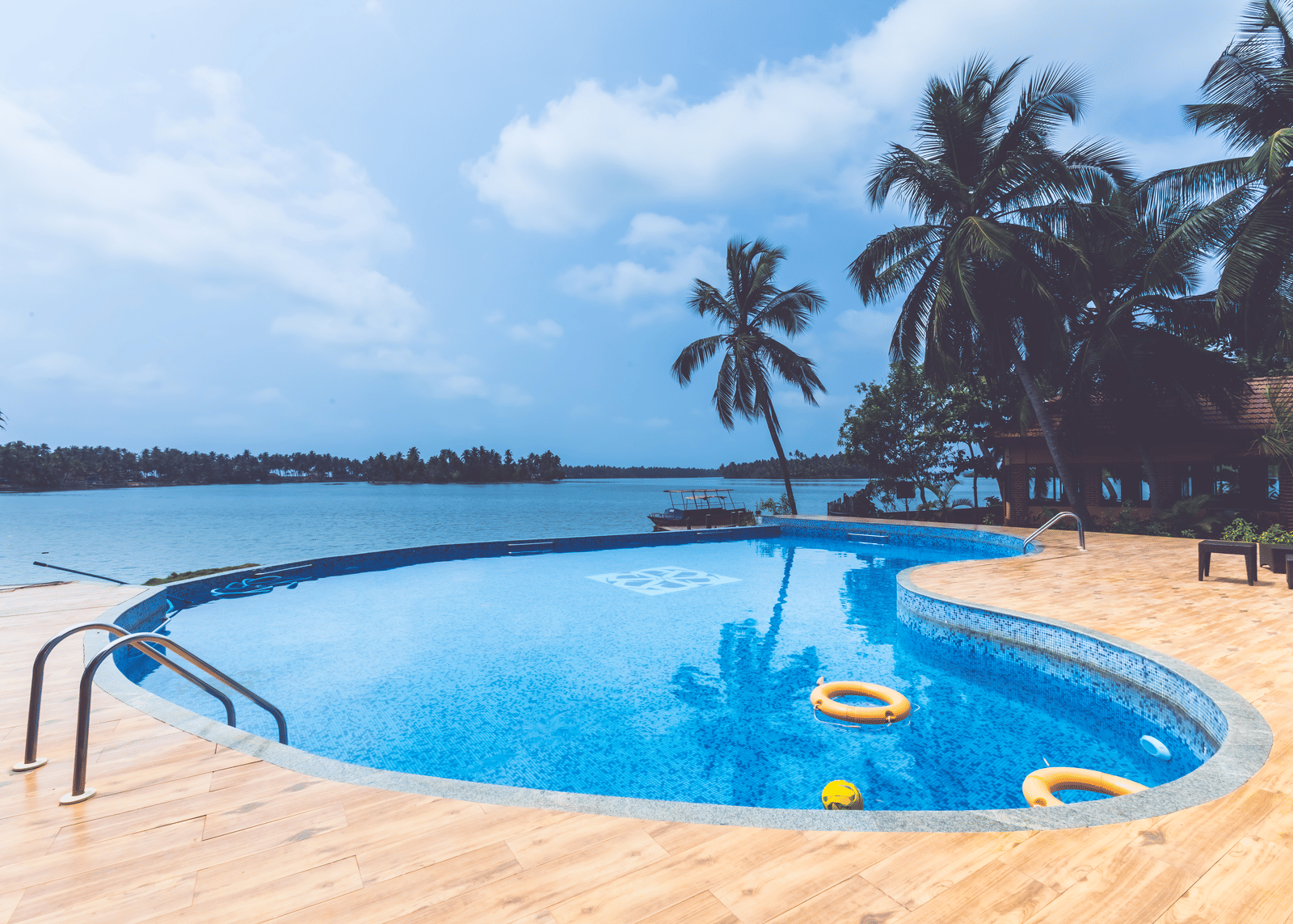 Swimming pool with pool floats, surrounded by palm trees and open sky at Paradise lagoon Resort, Udupi.