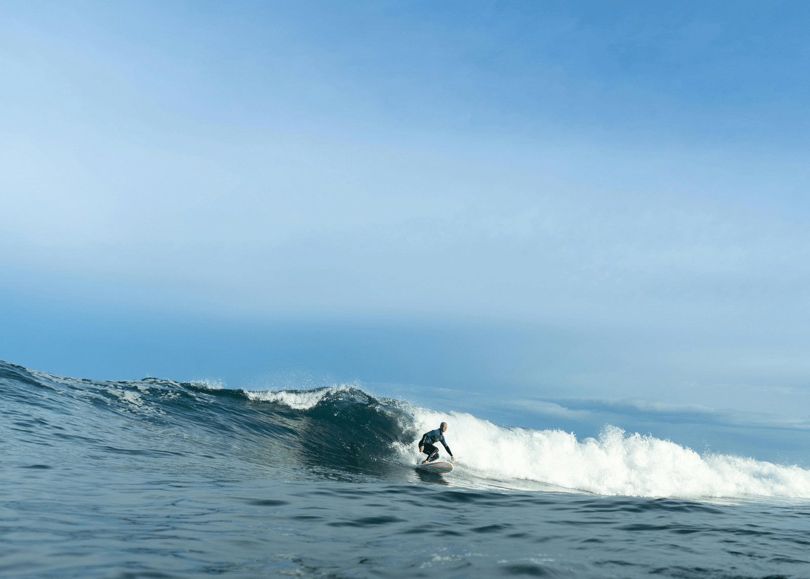 Surfer riding a wave in the ocean with blue water and clear sky in the background.