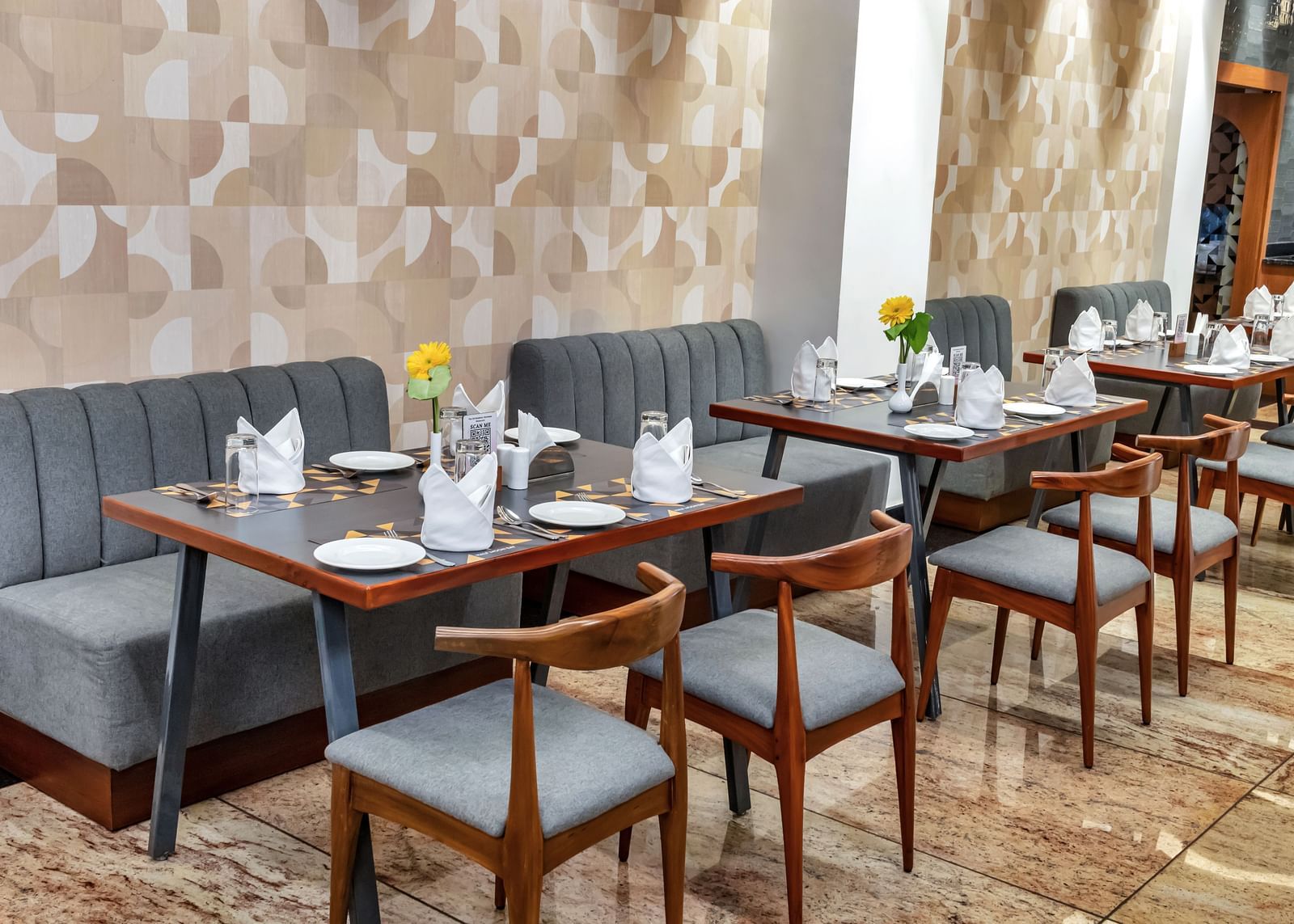 A well-lit restaurant dining area with multiple tables set with plates, cutlery, napkins, and flowers, along with comfortable seating against a patterned wall  | The Citi Residenci Hotel Banskopa