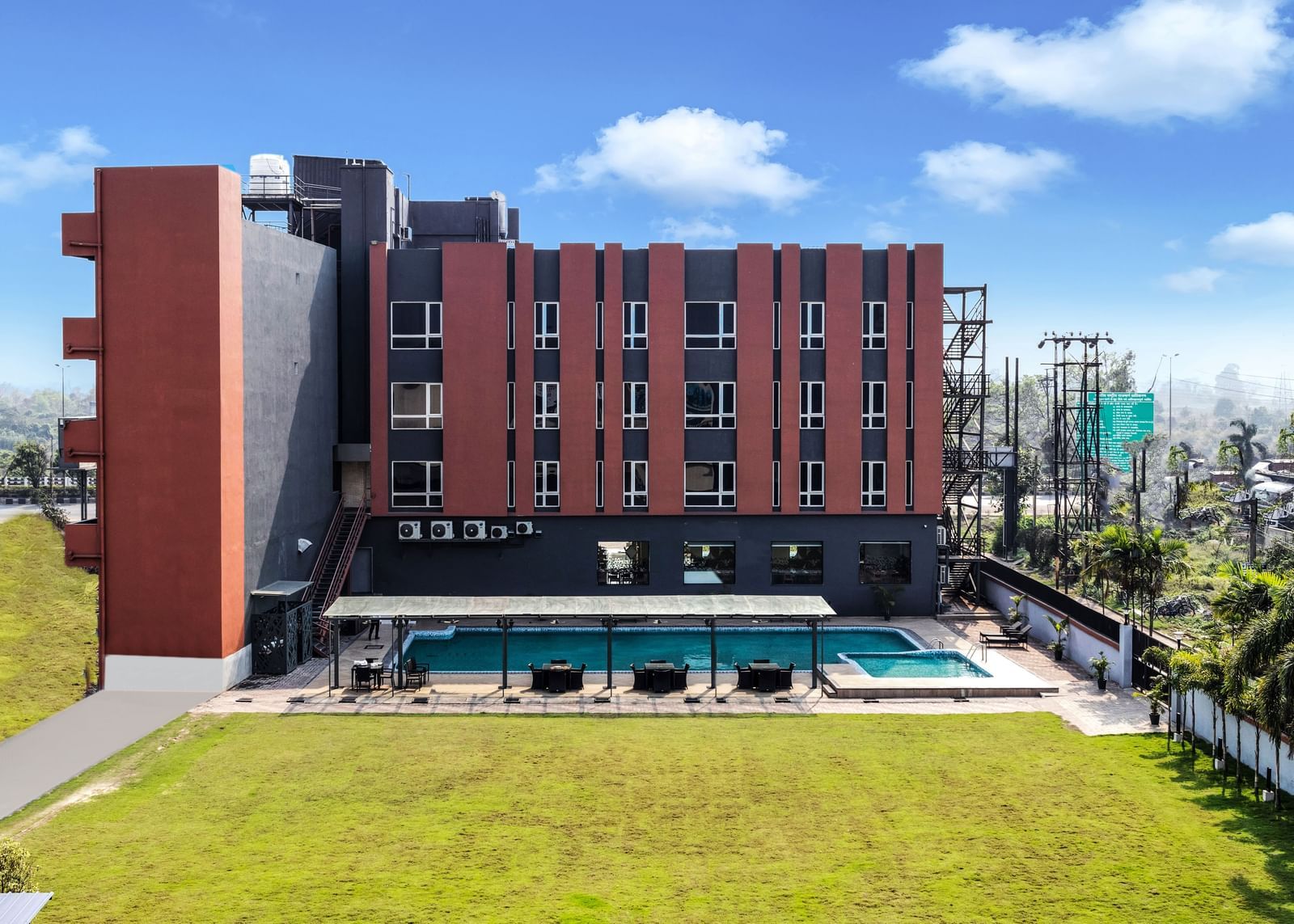 A modern hotel building with a swimming pool and green lawn under a partly cloudy sky | The Citi Residenci Hotel Banskopa