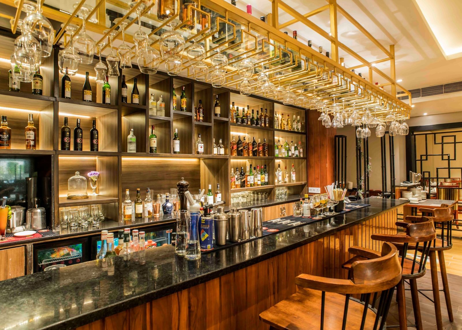 Well-stocked hotel bar with a dark countertop, multiple stools, and illuminated liquor bottles | The Citi Residenci Hotel Durgapur