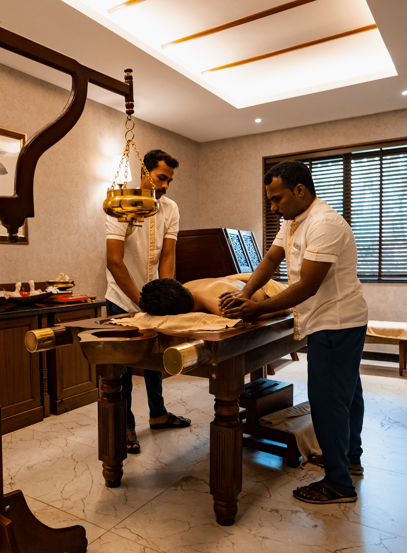 Two masseurs performing Abhyanga on a guests who is sleeping face down on a massage table - Gamyam Resort