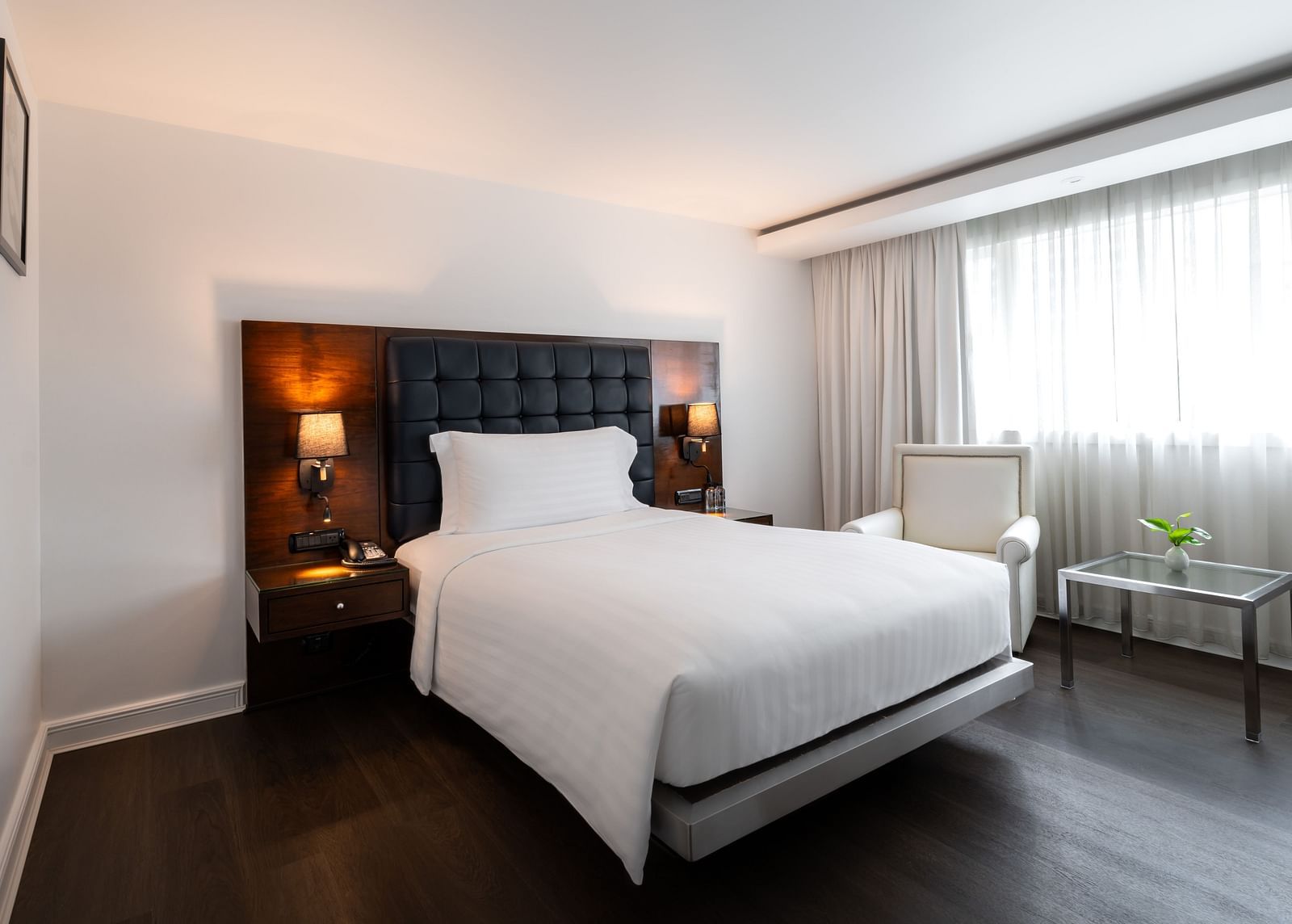 Minimalist bedroom with dark headboard, white linens, and window seating at Night Hotel Bangkok.