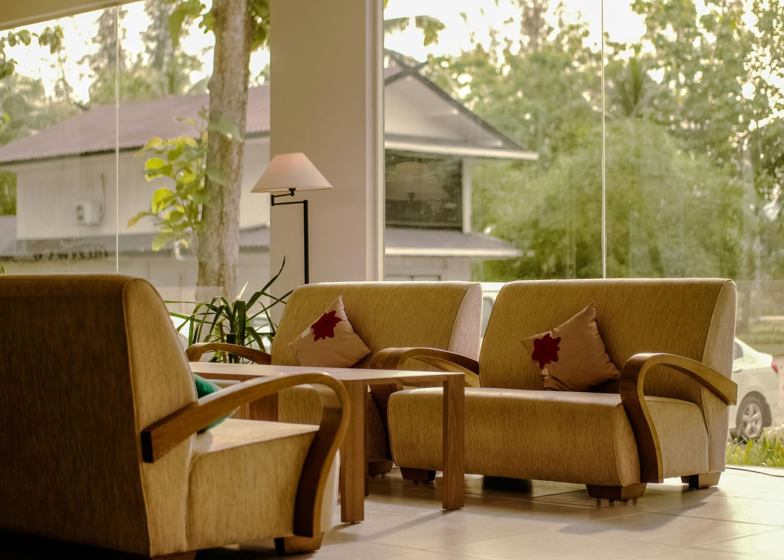 Comfortable seating area with beige armchairs, a small table, and decorative pillows near large windows overlooking greenery and buildings.