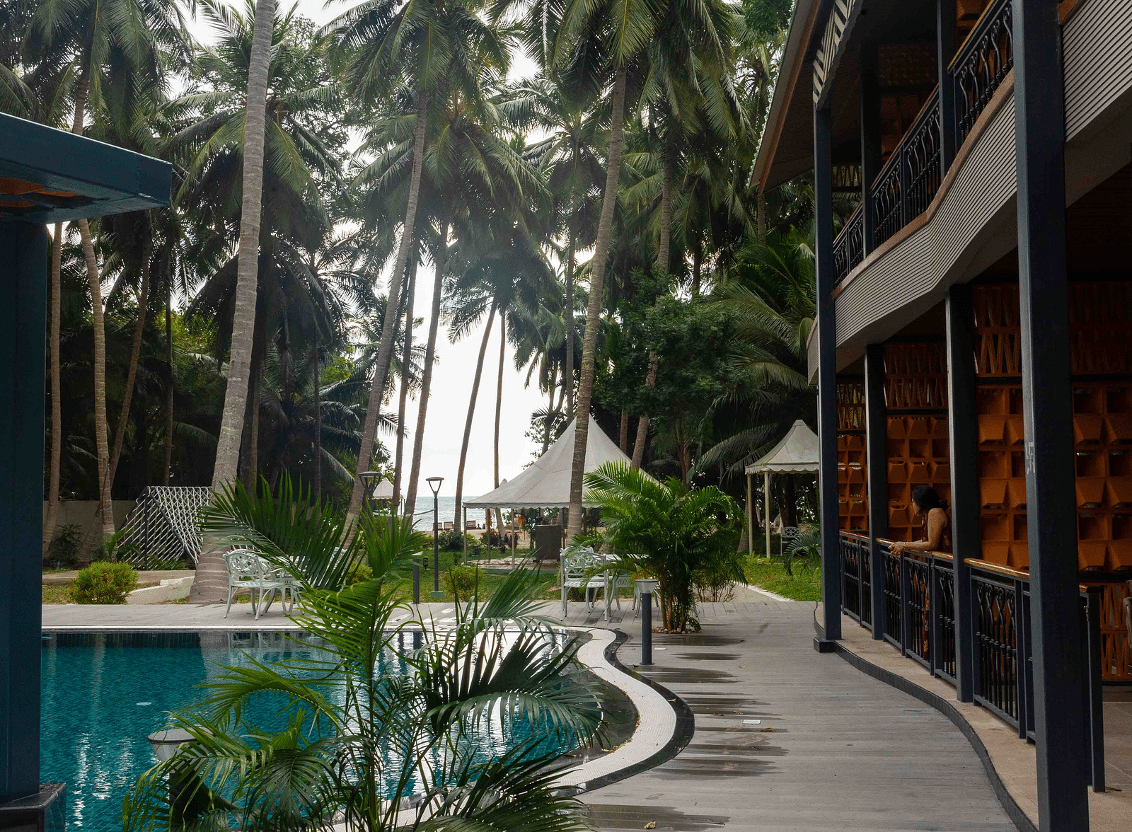A view of a modern pool area with tropical palm trees surrounding the space. The architecture of the building is visible, providing a relaxing and elegant setting - Coral Reef Resort & Spa, Havelock