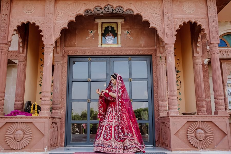 A bride in a traditional outfit adjusts her attire in front of a decorated door -  Umaid Palace - Best Luxury Heritage Resort Near Jaipur
