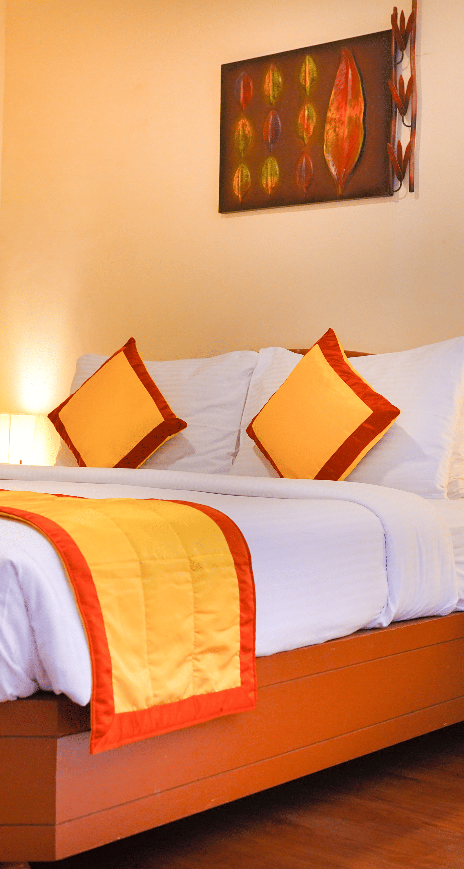 A well-appointed bedroom with a large bed, a yellow and orange bed runner, two bedside lamps, and a decorative wall hanging at La Montana By TGI, Ooty