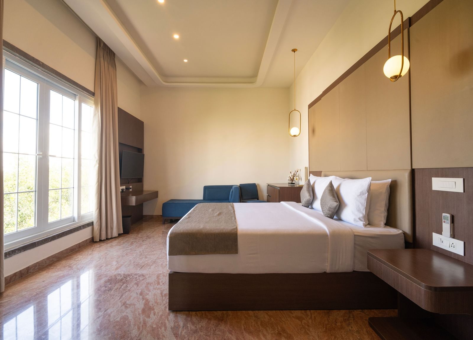 A chennai hotel room featuring a king size bed, a seating area, hanging lights and french windows filtering natural light through french windows - Accord Chrome Airport Hotel
