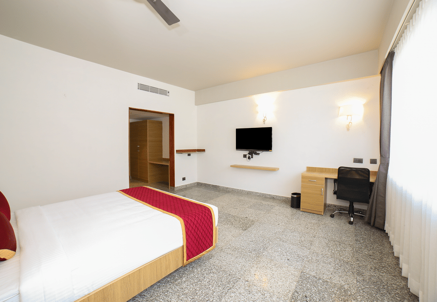 A double bed, a wooden desk with a chair, and a wall-mounted television at Icon Express By Bhagini, Mahadevapura.