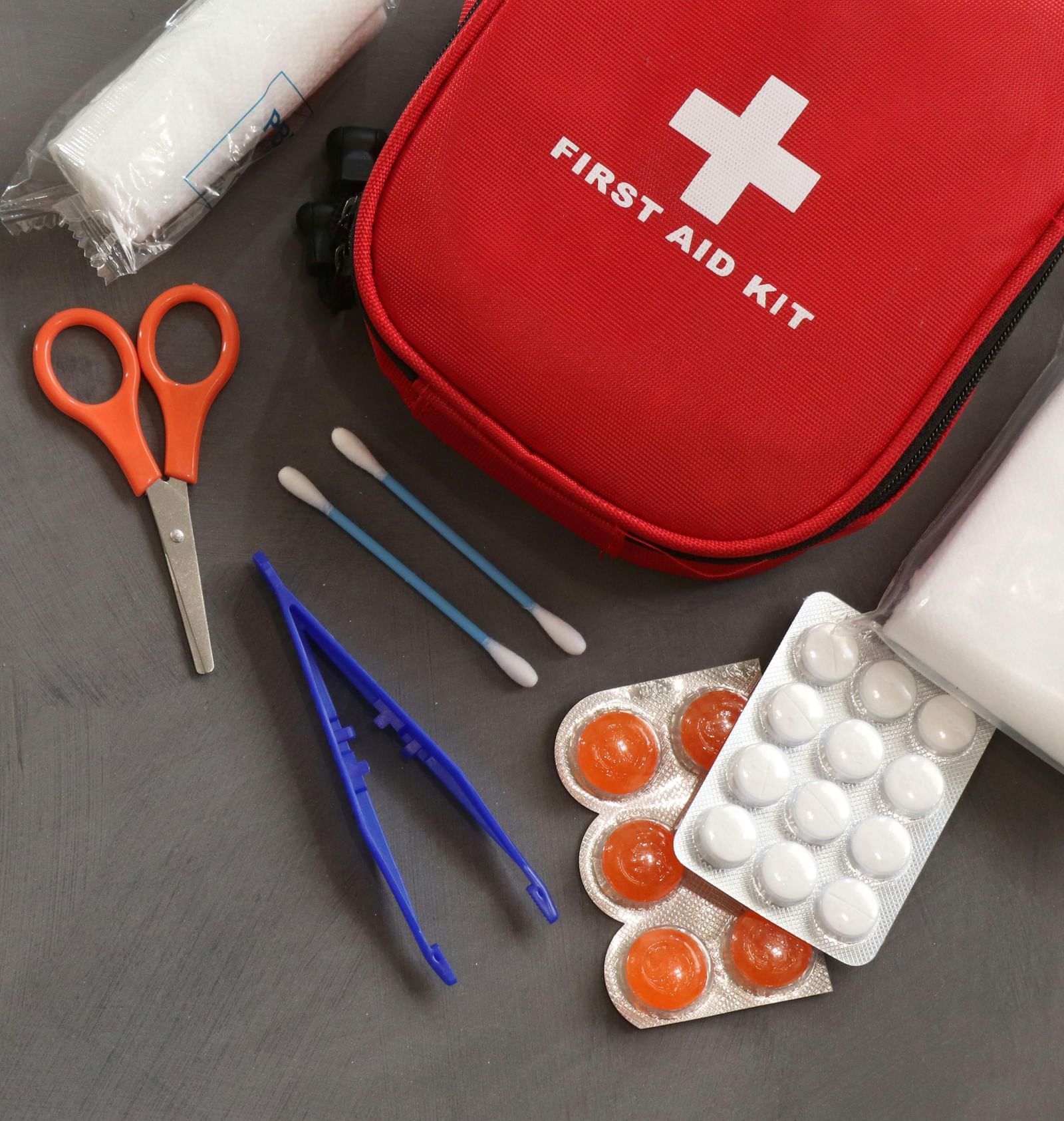 A red coloured pouch reading 'First Aid Kit' with several items and medicines scattered around it.