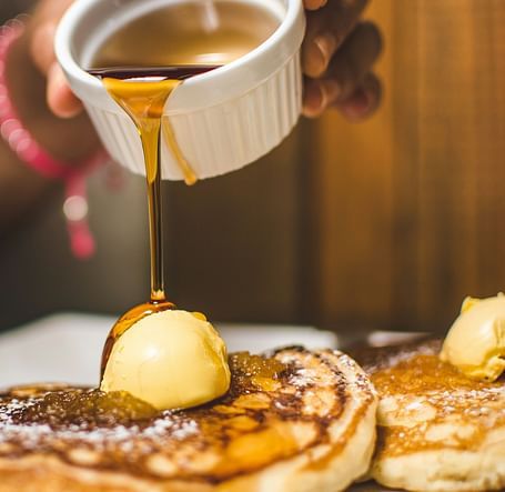 Syrup being poured over a stack of fluffy pastries.