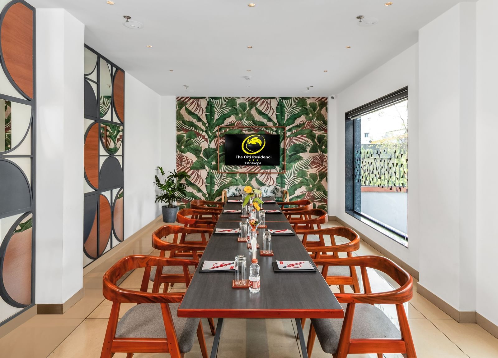 A modern meeting room with a long table, wooden chairs, a tropical-themed wallpaper, and a wall-mounted screen | The Citi Residenci Hotel Banskopa