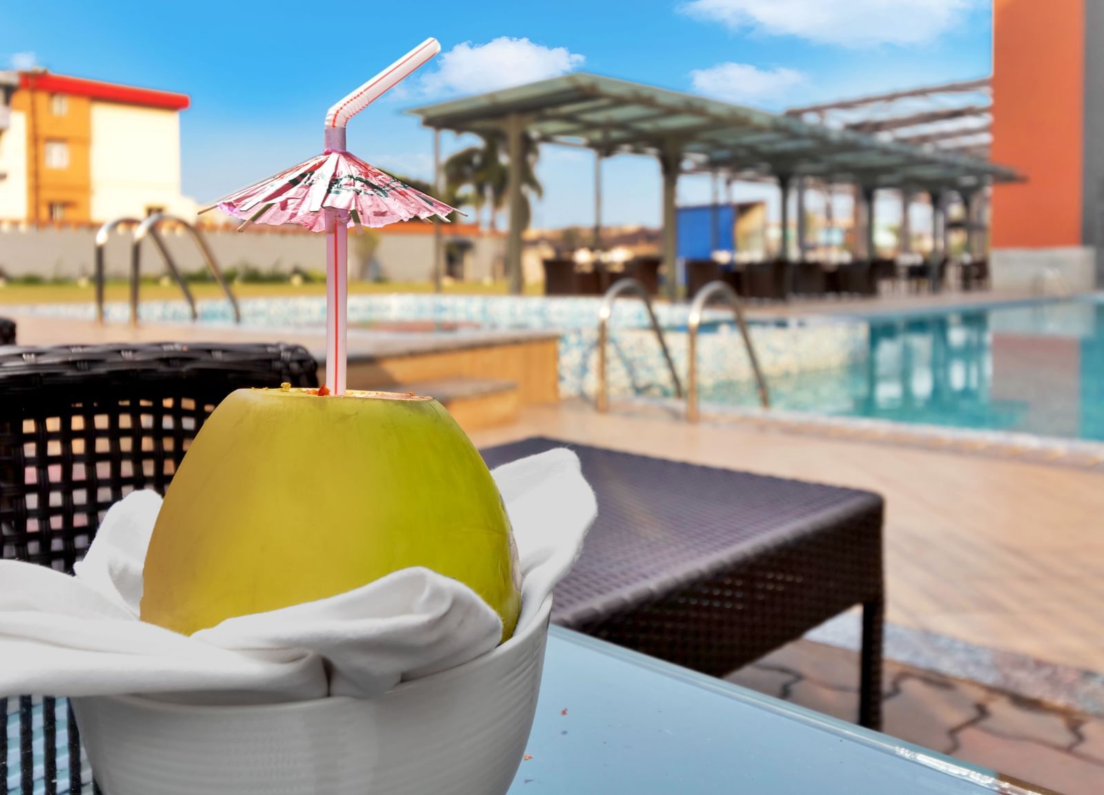 A refreshing drink in a coconut shell with a straw and umbrella, by a swimming pool | The Citi Residenci Hotel Banskopa