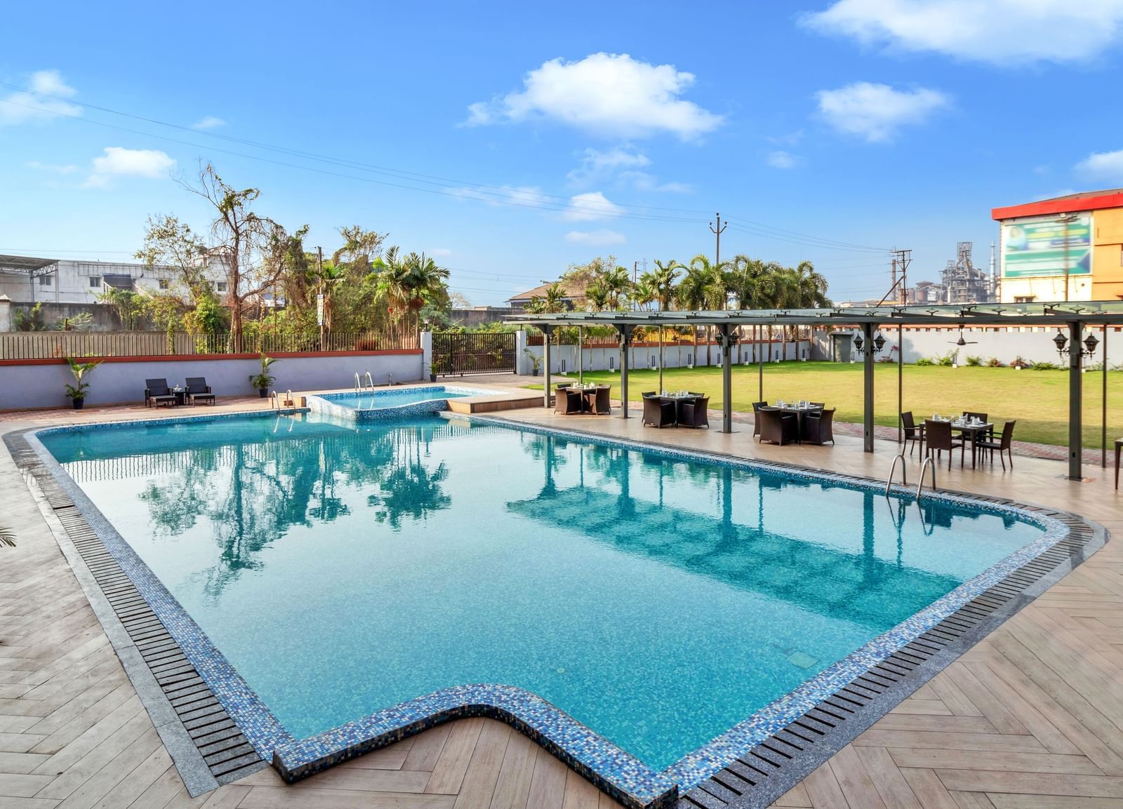 A large outdoor swimming pool with clear blue water, surrounded by lounge chairs and covered seating areas on a sunny day | The Citi Residenci Hotel Banskopa