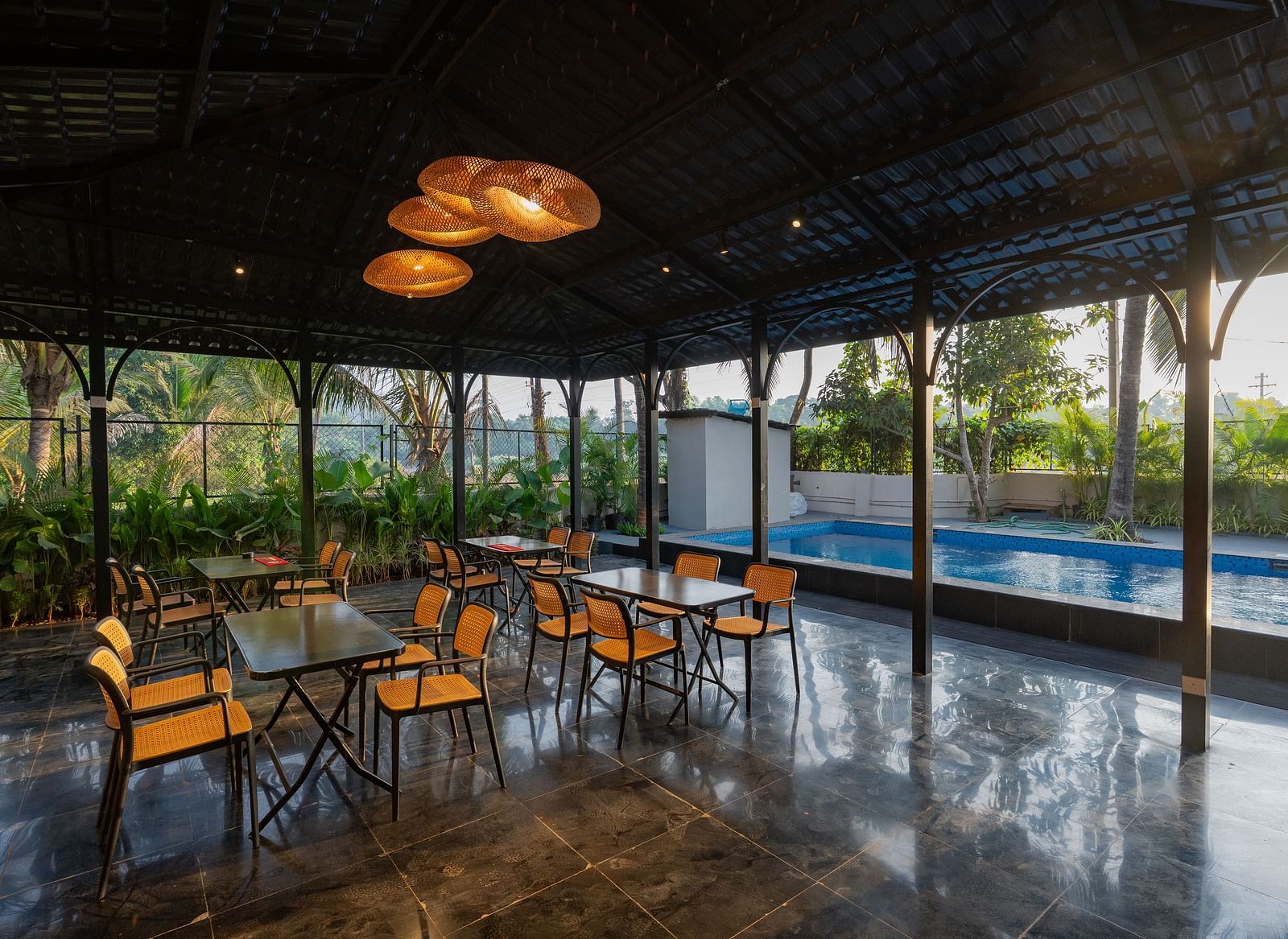 Covered open-air dining area with tables and chairs, overlooking a swimming pool and lush greenery at Kssemya.