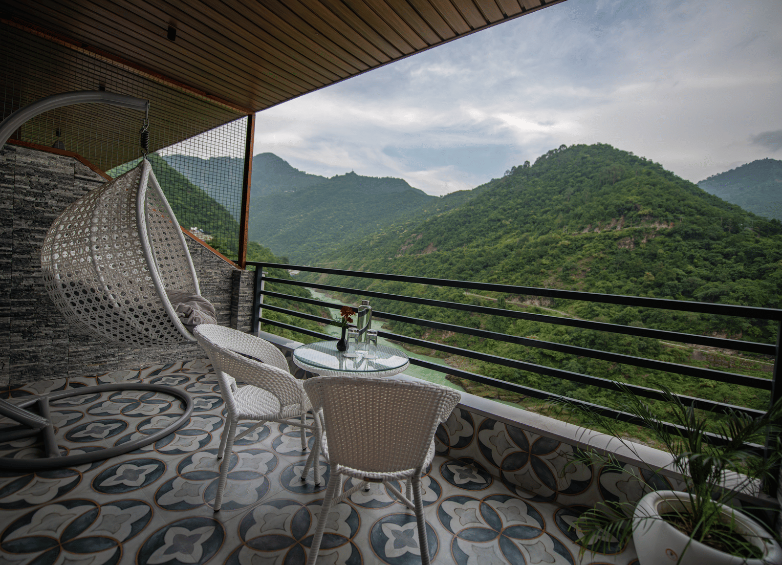 Balcony at The Tattva Devaprayag with two white chairs and a table overlooking the mountains and flowing river.